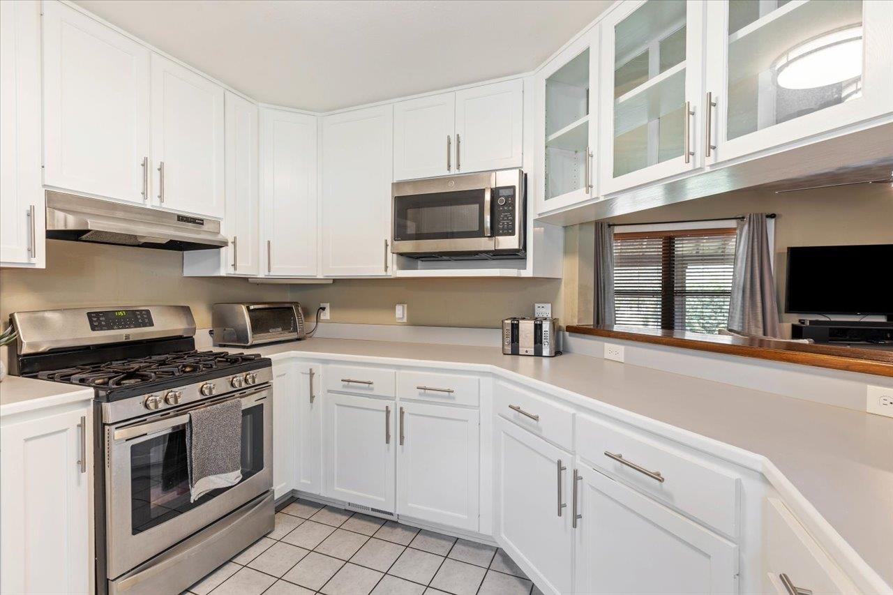 Kitchen with white cabinets, stainless steel gas range, and a long counter beneath a pass-through.