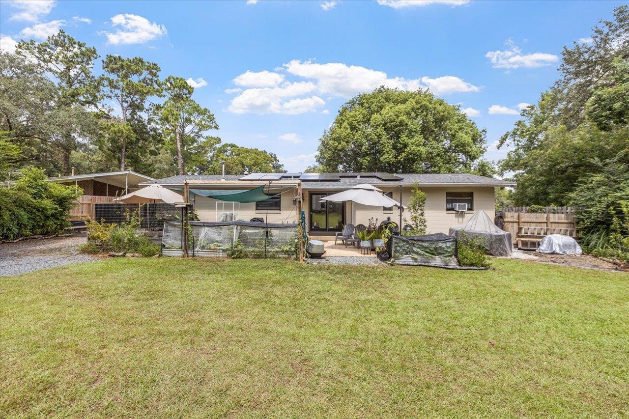 Single-story home with solar panels, patio seating, umbrellas, and a broad backyard lawn.