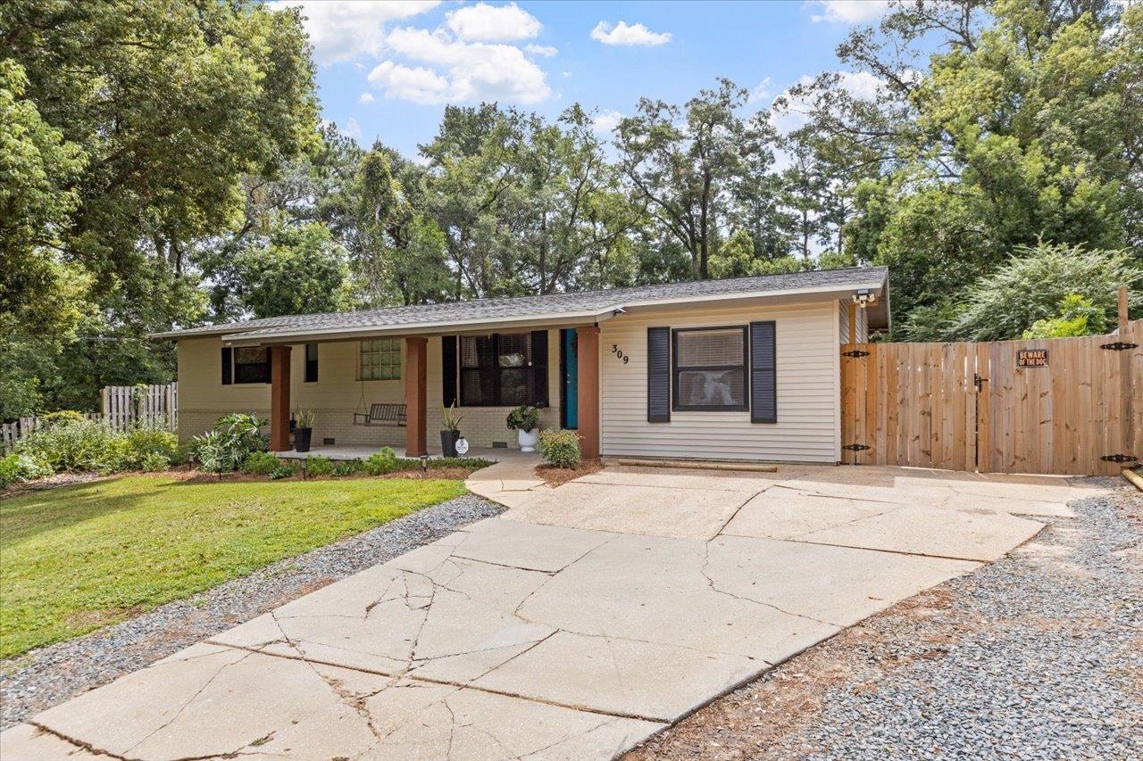 Single-story home with a covered porch, wide concrete driveway, and tall wooden gate.