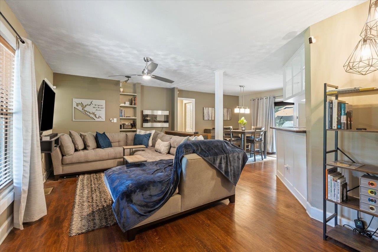 Living room with a beige sectional, dark blue throws, hardwood floors, and an open dining area.