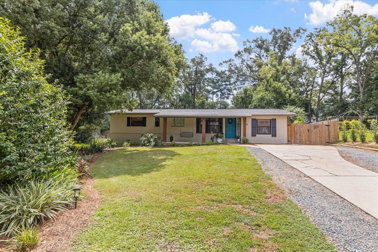 Single-story home with a turquoise front door, broad lawn, paved driveway, and mature trees.