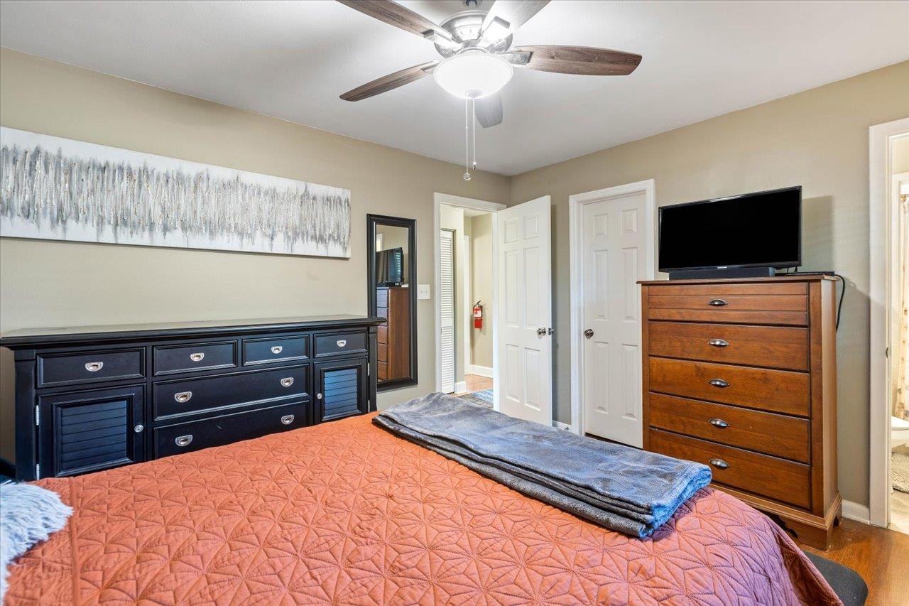 Furnished bedroom with a coral quilted bed, dark dresser, and ceiling fan.