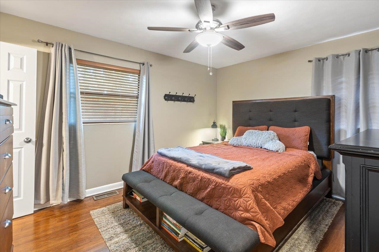 Bedroom with a rust-colored quilt, dark upholstered headboard, and ceiling fan.