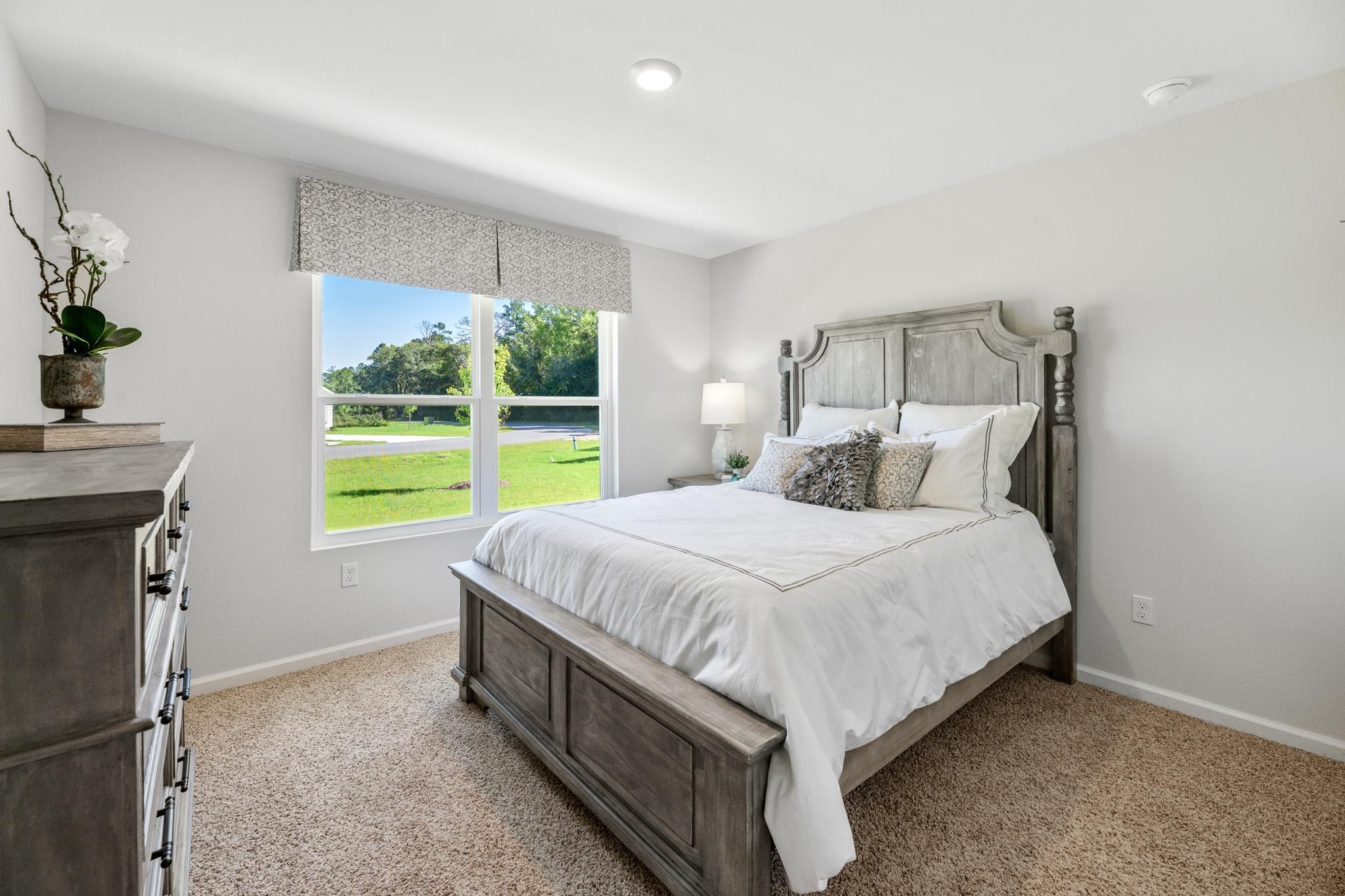 Bedroom with a gray wood bed, white bedding, and a large window overlooking a green lawn.