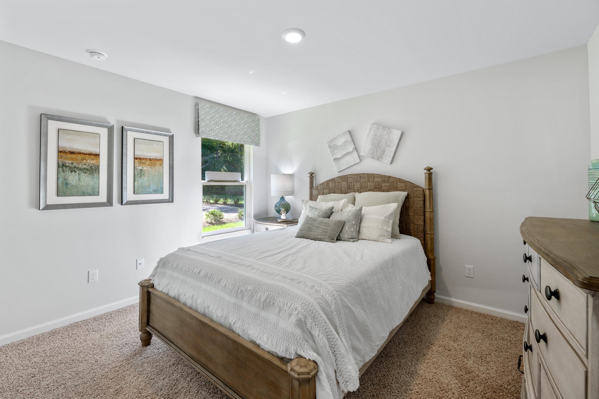 Bright bedroom with a white bed, woven wood headboard, and window overlooking greenery.