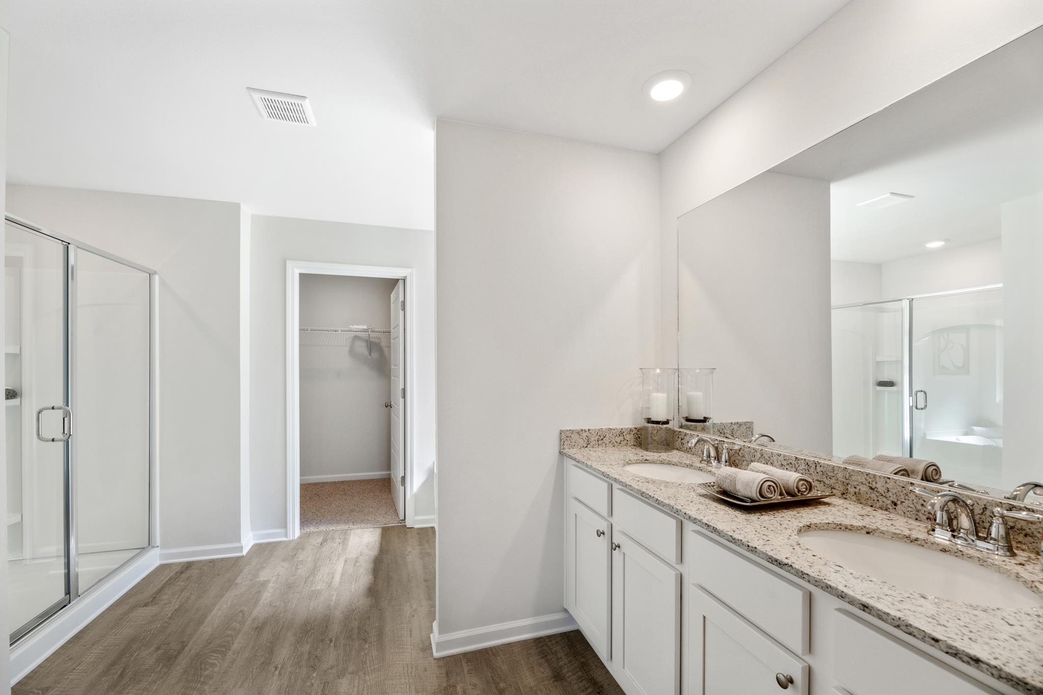 Bathroom with a double-sink granite vanity, large mirror, glass shower, and open walk-in closet.