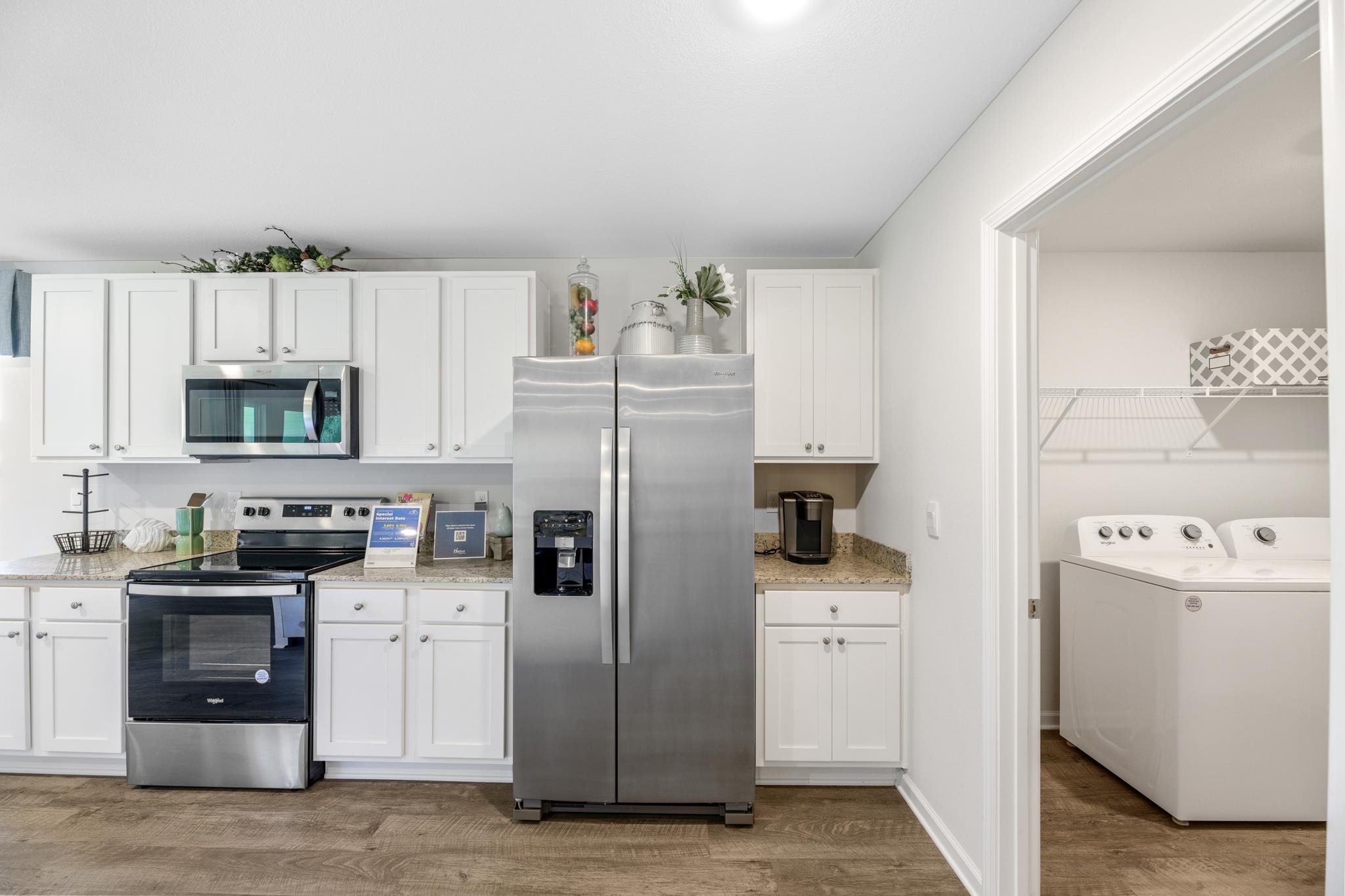 Kitchen with white cabinets and stainless steel appliances, opening to a laundry room with washer and dryer.