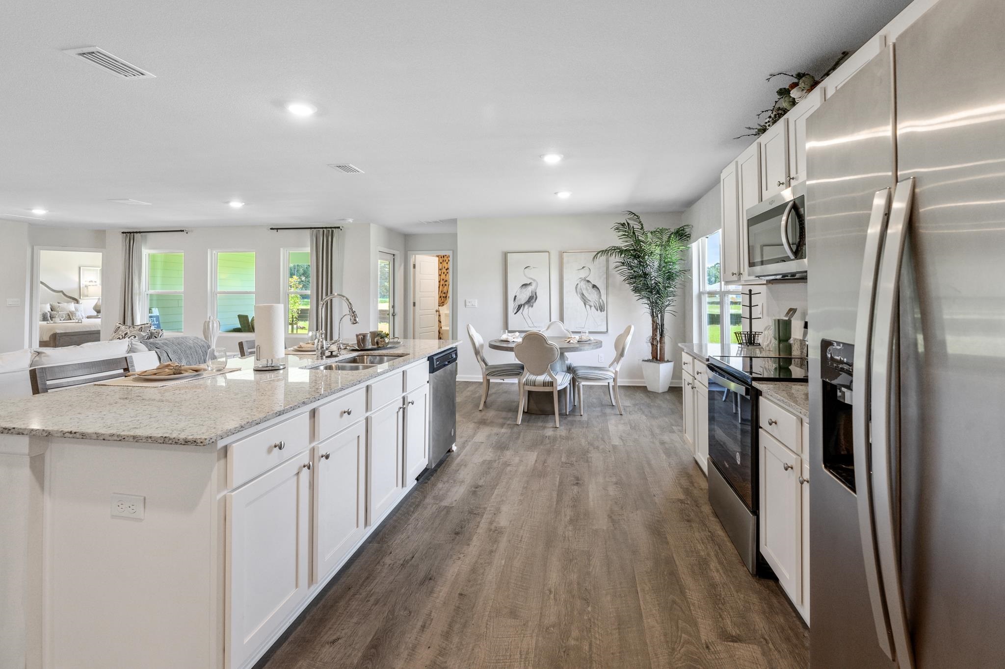 Open-plan kitchen with a large stone island, stainless steel appliances, and a dining area by the windows.