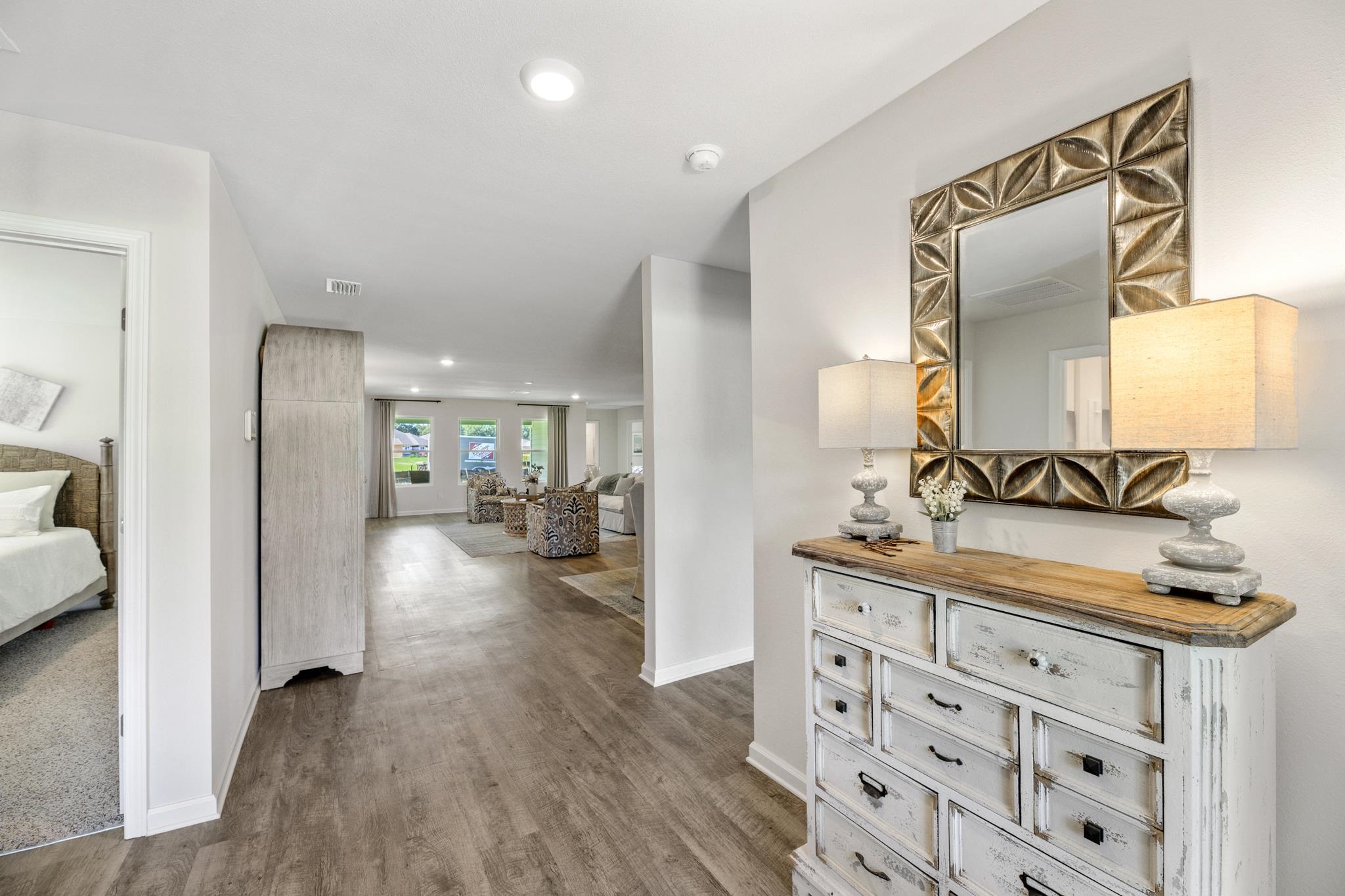 Staged entry hall with a distressed white dresser and bronze-framed mirror, opening to a furnished living room.