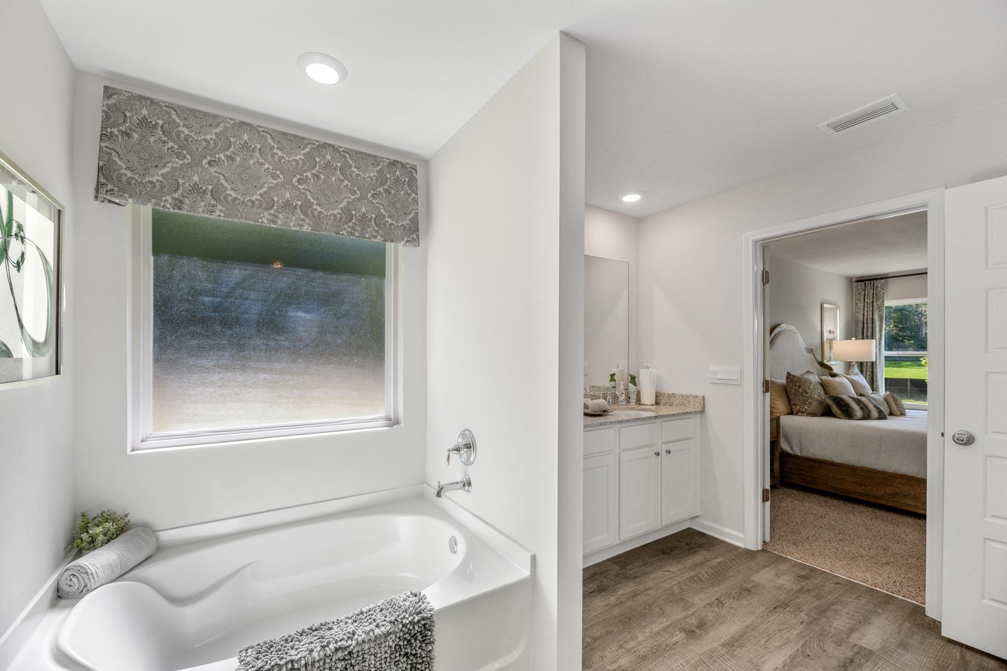 Bathroom with a soaking tub, patterned window shade, and doorway to a bedroom.