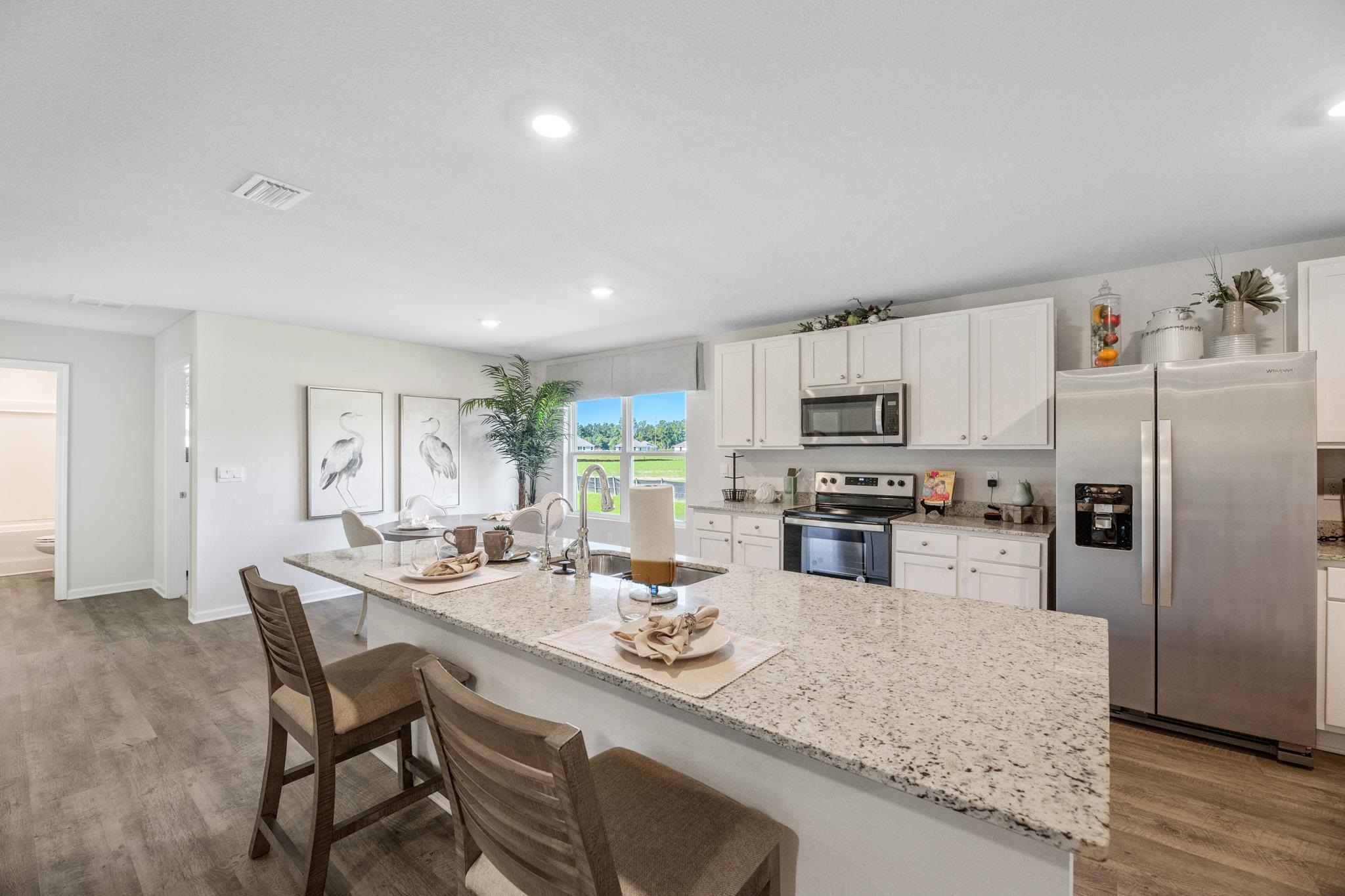 Kitchen with a large granite island, white cabinets, stainless steel appliances, and a window-side dining nook.