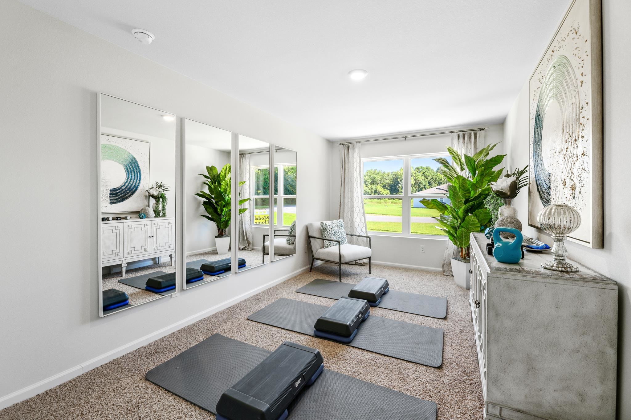 Bright home gym with mirrored wall, exercise mats, step platforms, and a large window.