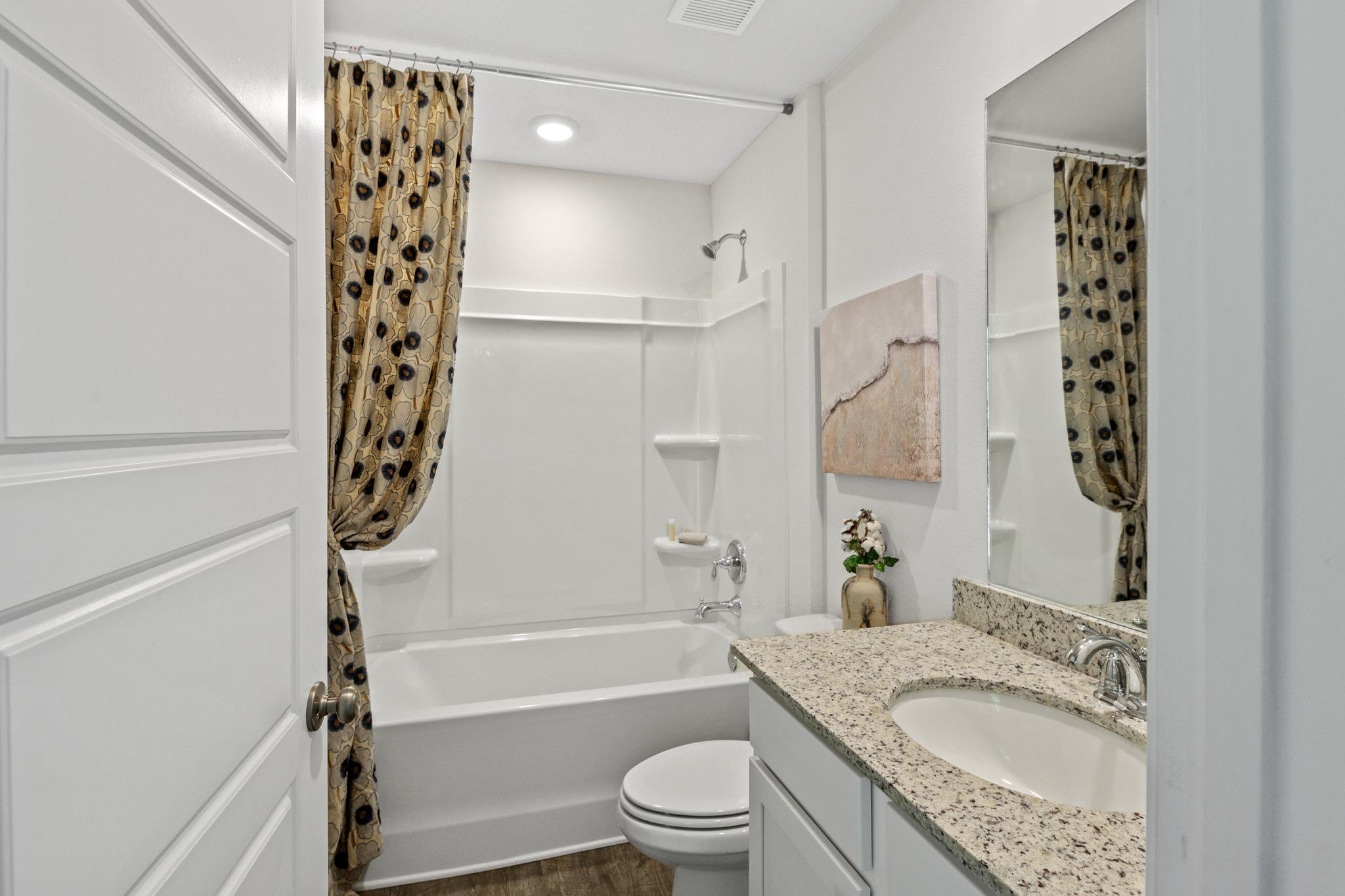 Bathroom with a granite vanity, bathtub, and patterned shower curtain.