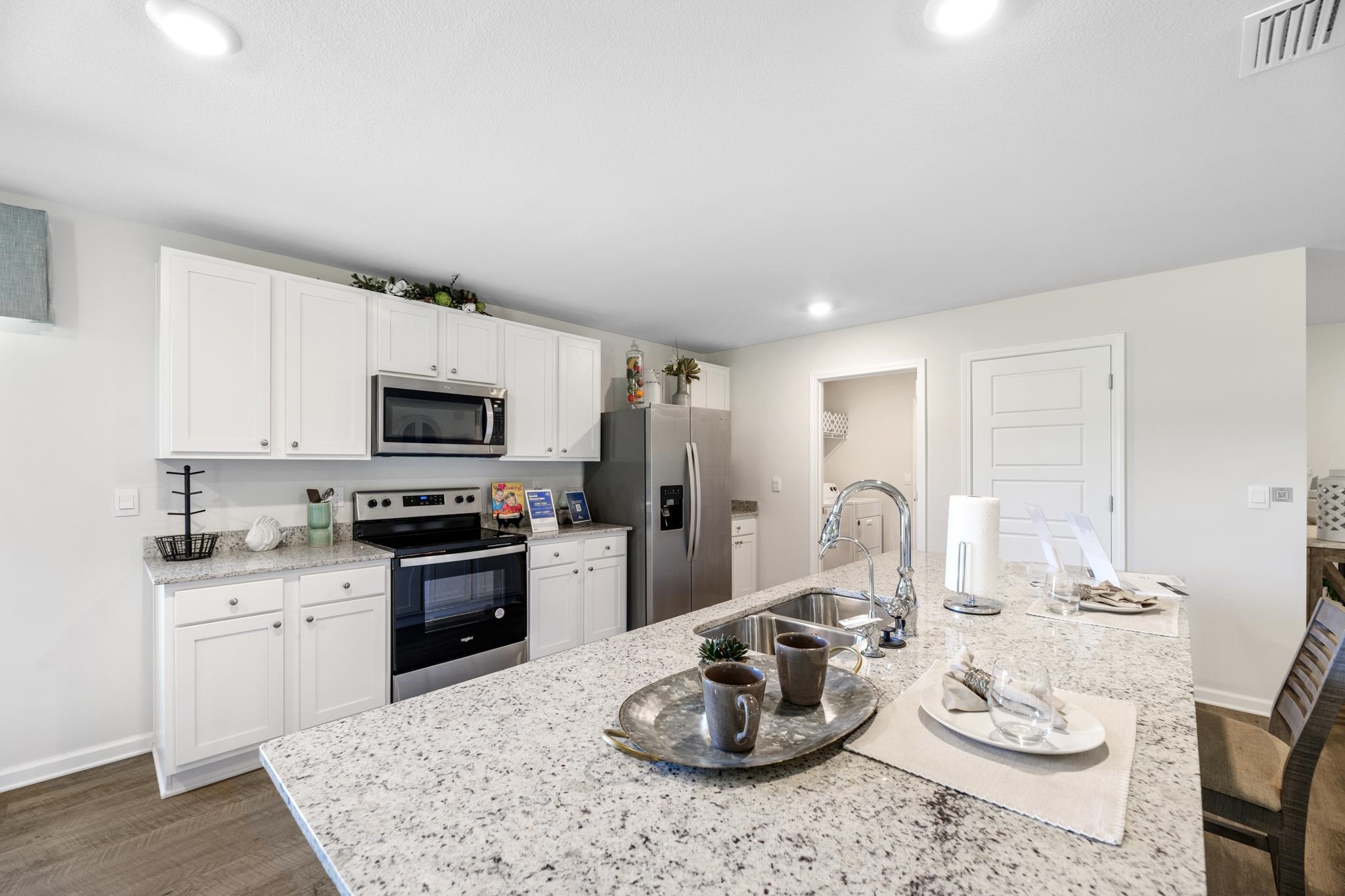 Staged kitchen with a granite island, white cabinetry, and stainless steel appliances.