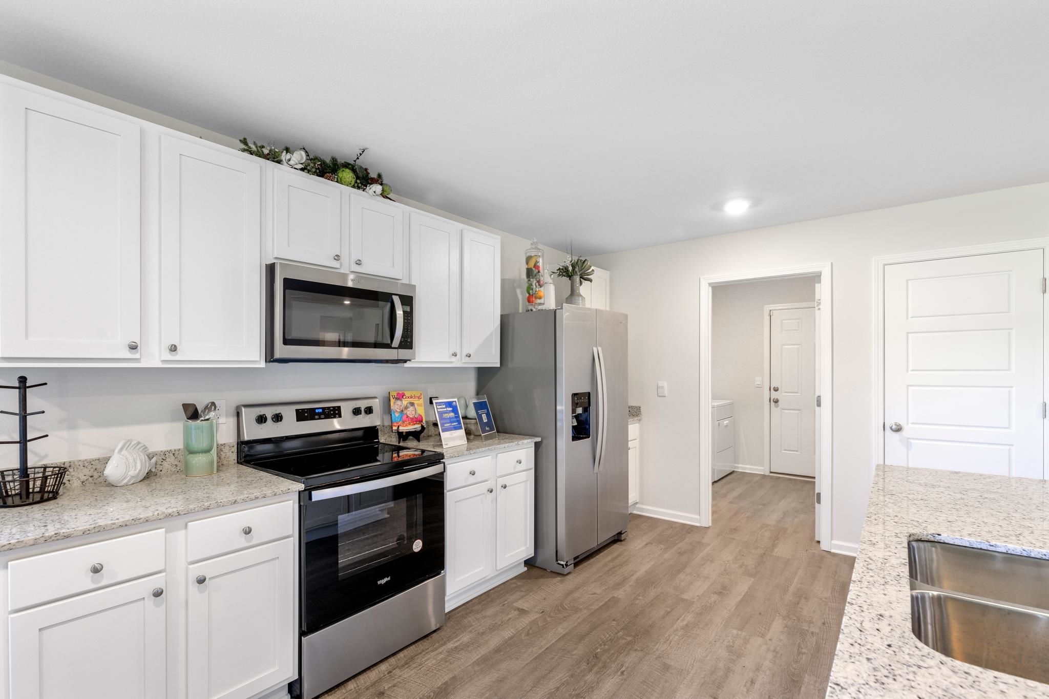 Bright kitchen with white cabinets, granite counters, stainless steel appliances, and wood-look flooring.