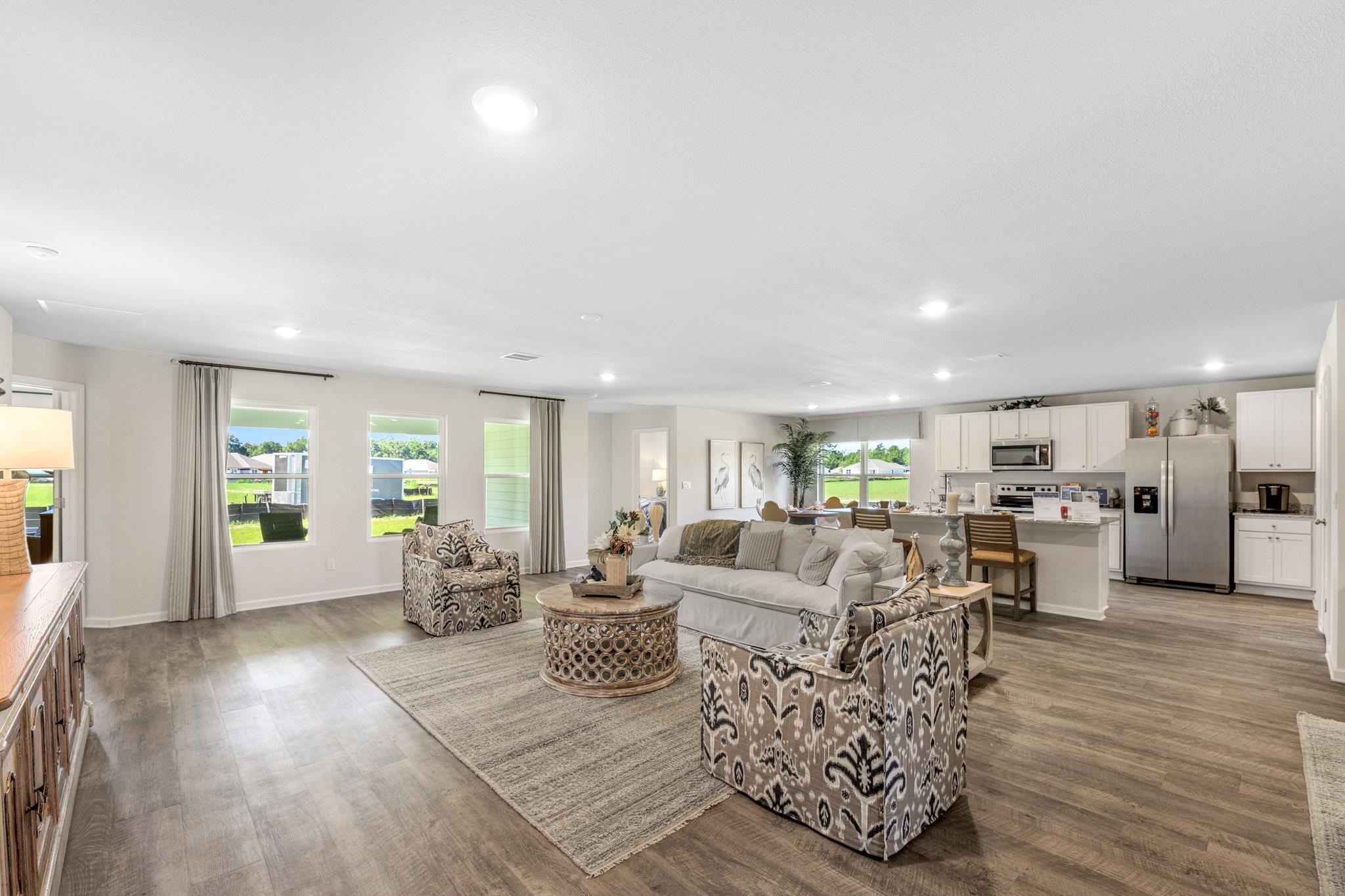 Open-plan living room and kitchen with patterned armchairs, white cabinetry, and stainless steel appliances.