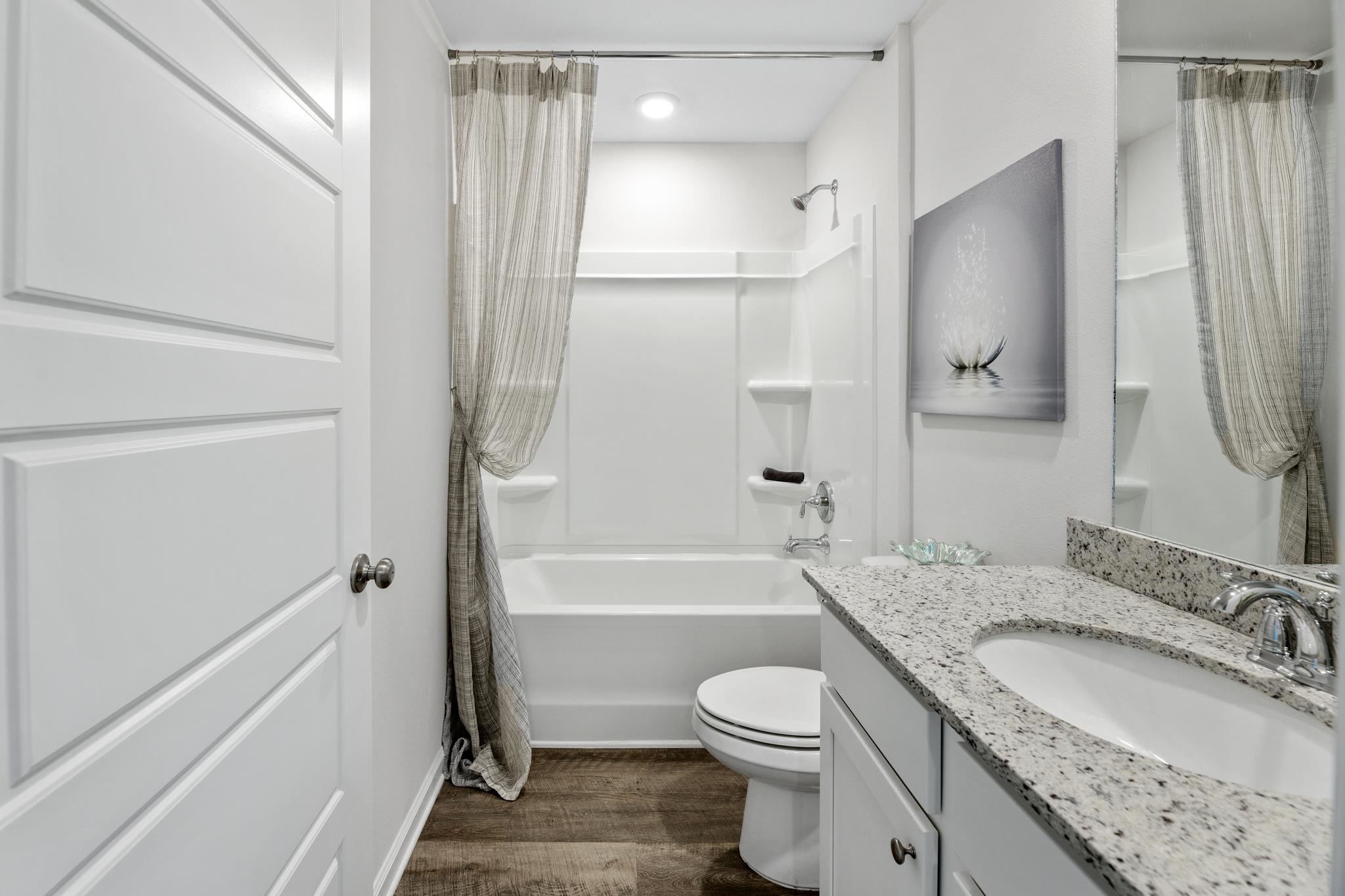 Bathroom with a curtained tub and shower, toilet, and granite-topped vanity.