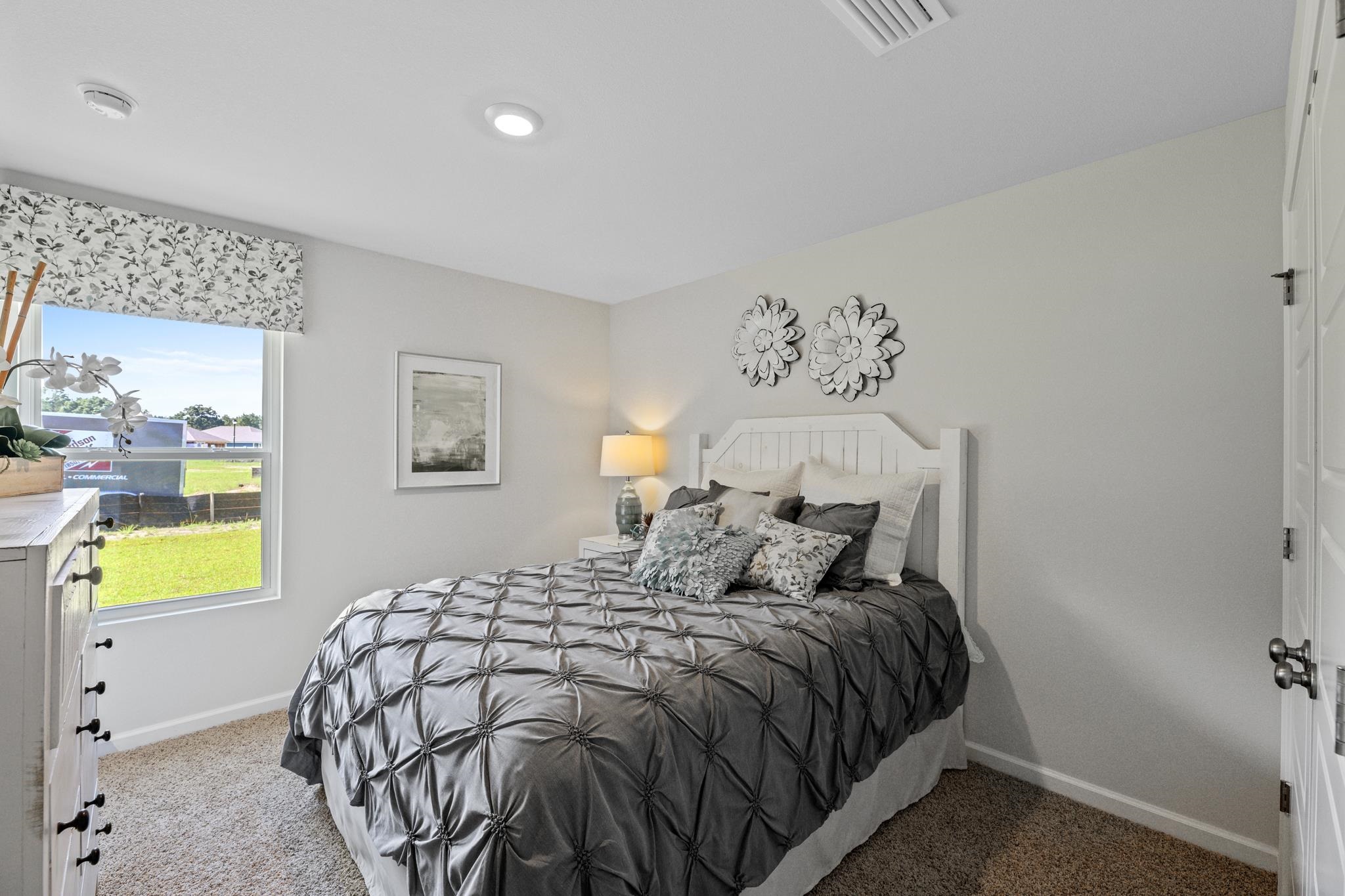 Furnished bedroom with a gray tufted comforter, white headboard, and large window.