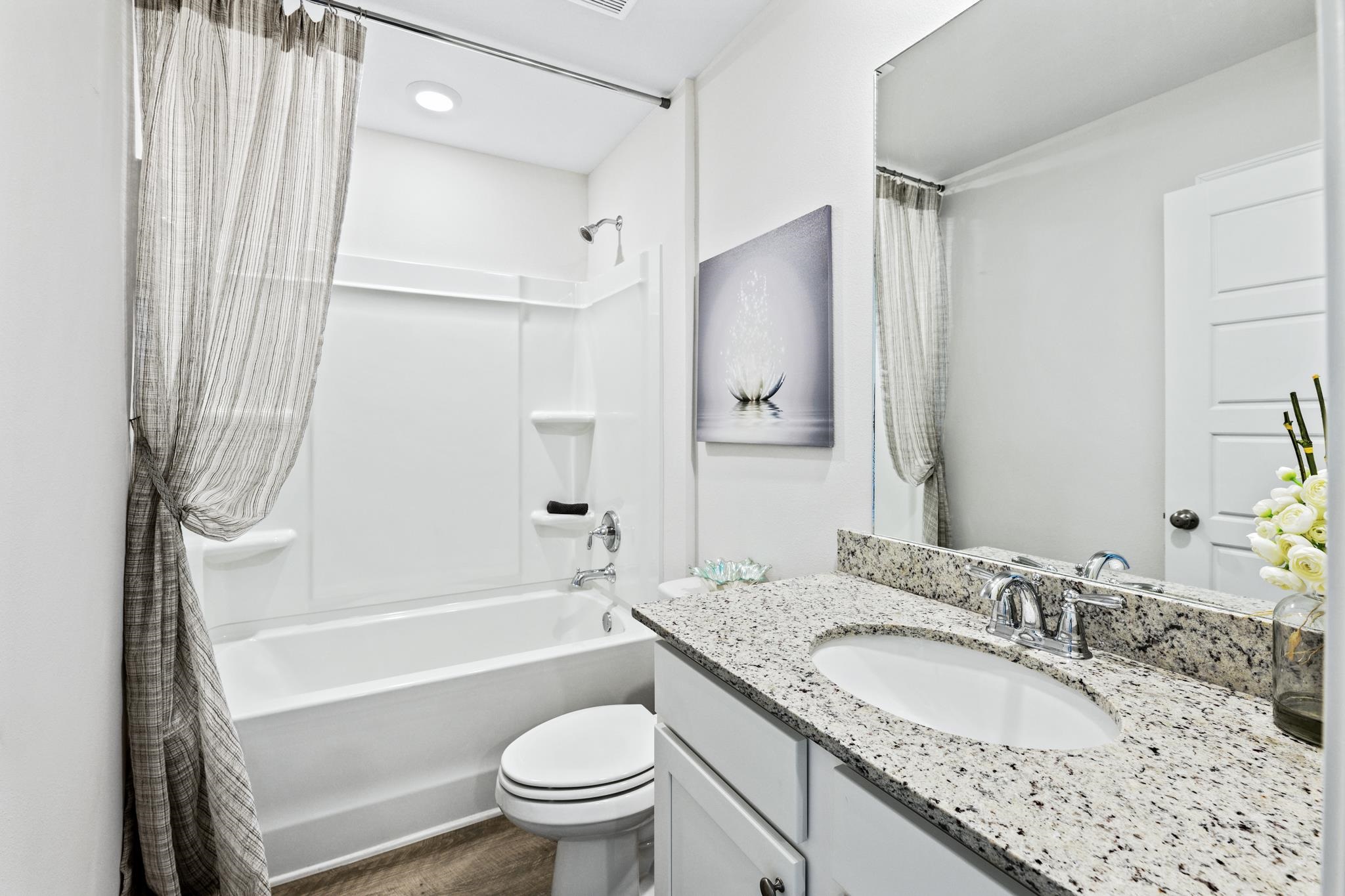 Bathroom with a granite vanity, oval sink, white tub, and gray sheer shower curtain.