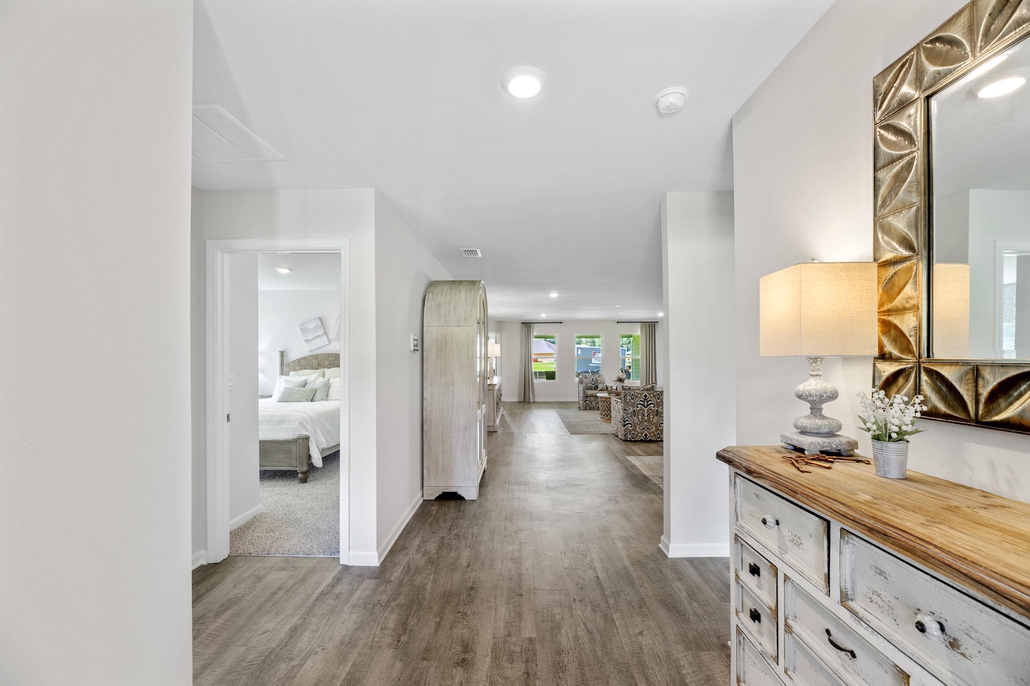 Bright entryway with wood-look floors, a decorative mirror and console, and a bedroom doorway.