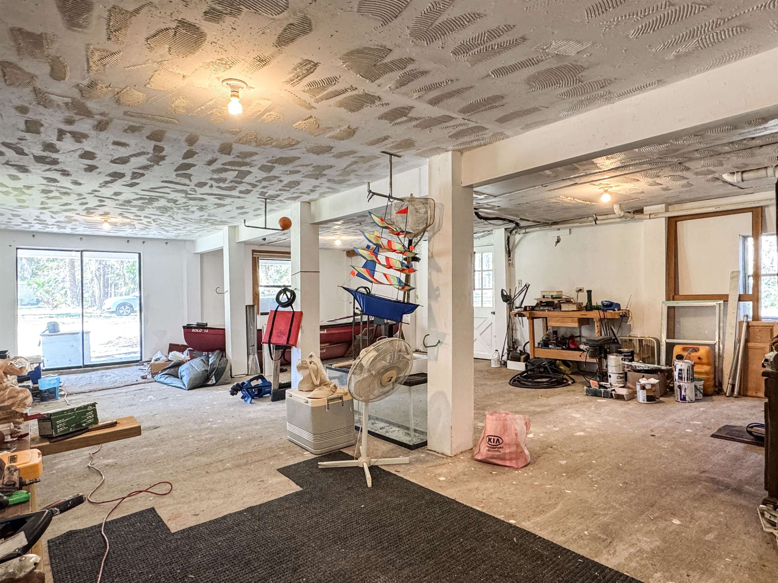 Unfinished room with boats, workshop tools, support columns, and a ceiling covered in joint compound.