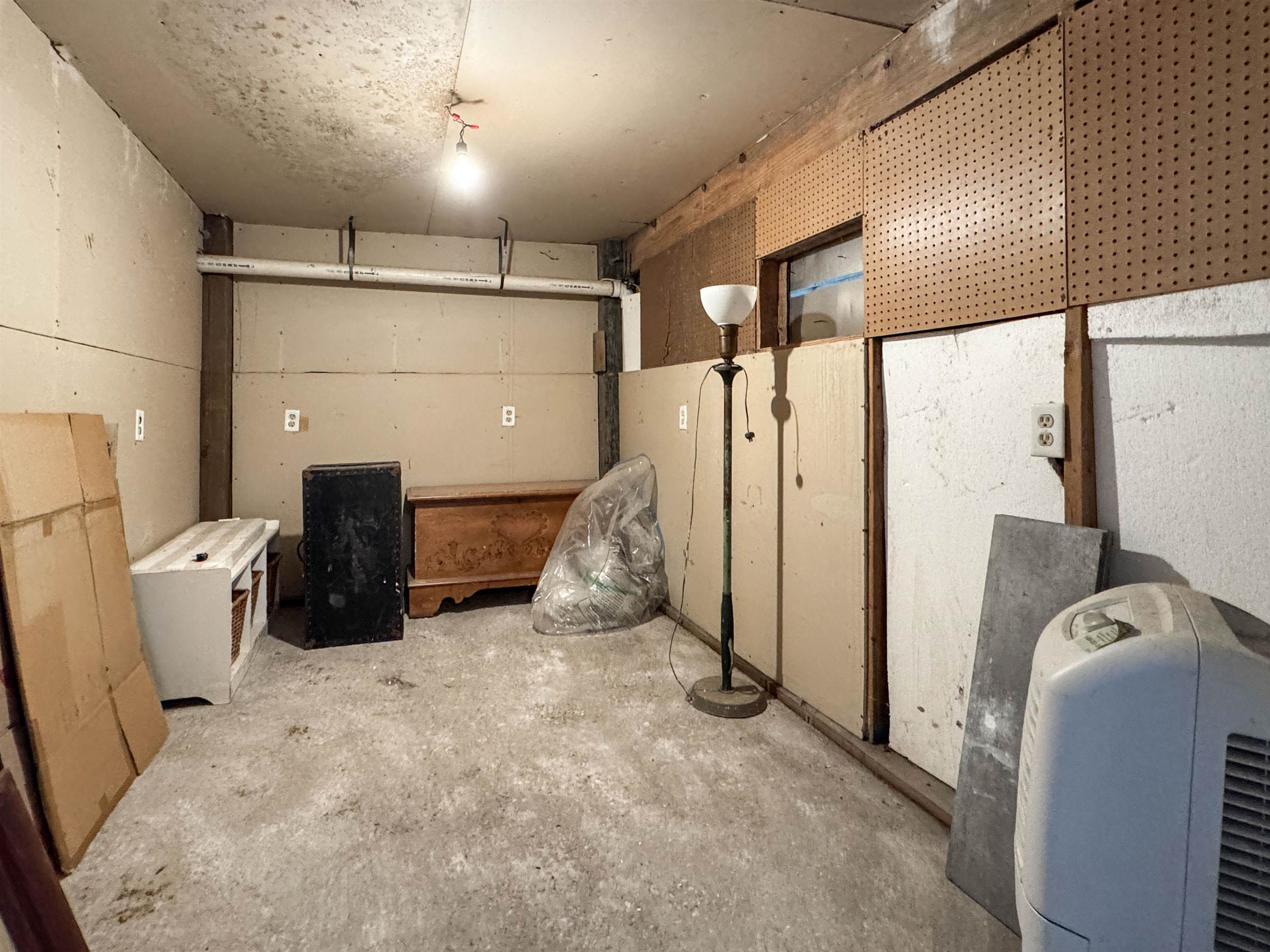 Unfinished storage room with pegboard walls, exposed pipes, and assorted stored items.