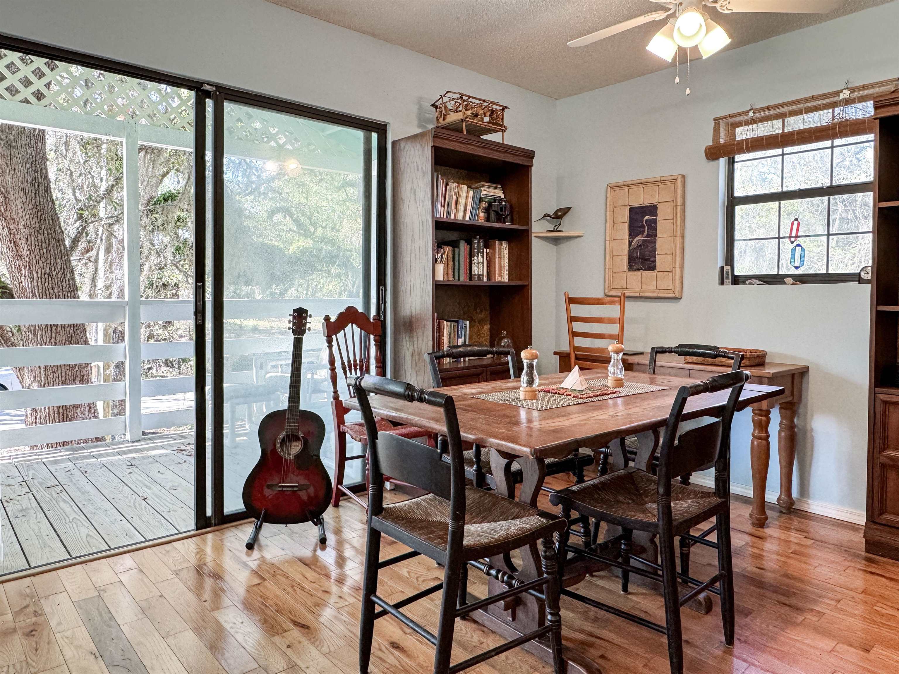 Dining room with a wooden table, bookcase, and guitar beside sliding glass doors to a deck.