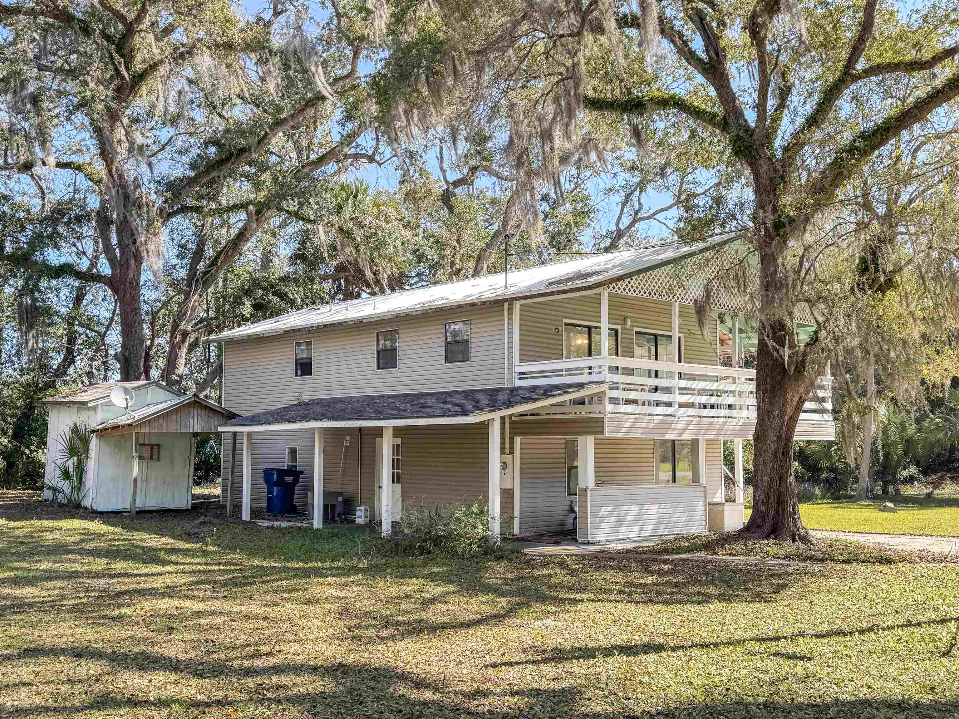Two-story home with a covered porch and balcony beneath moss-draped live oaks.