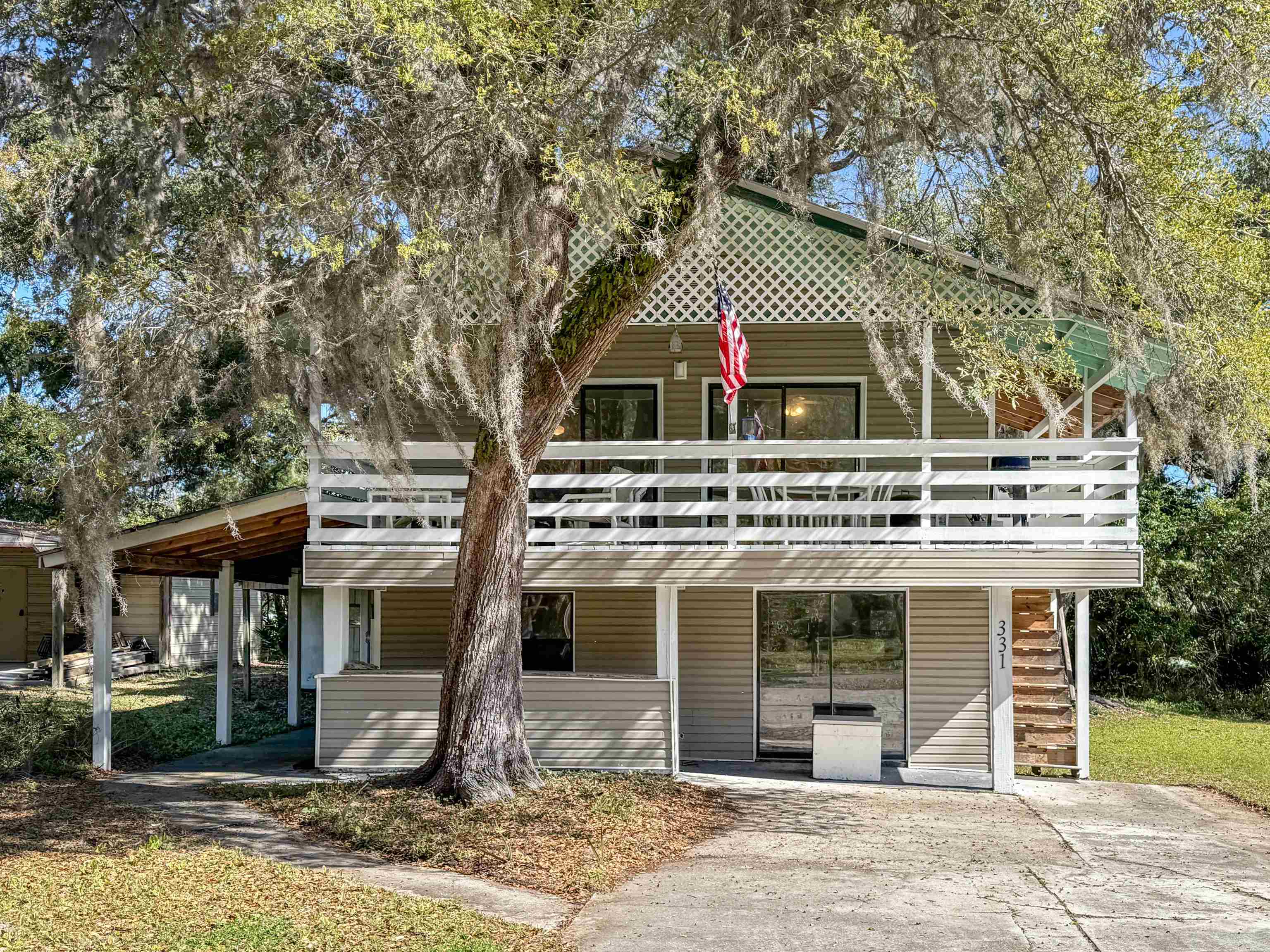 Two-story tan home with a white-railed porch, exterior stairs, and a large Spanish-moss-draped oak.