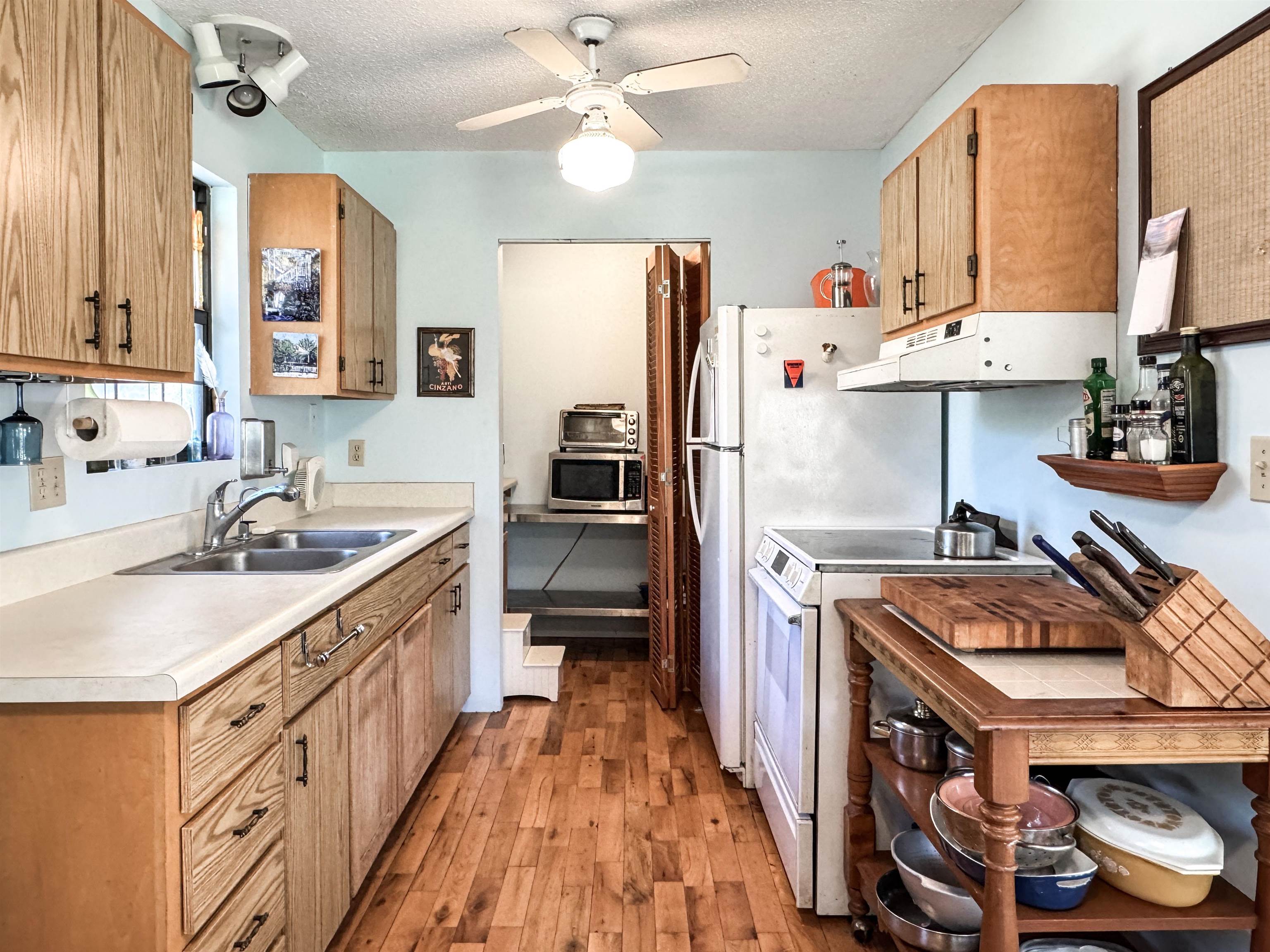 Kitchen with wood cabinets, a double-basin sink, white appliances, and a wooden worktable.