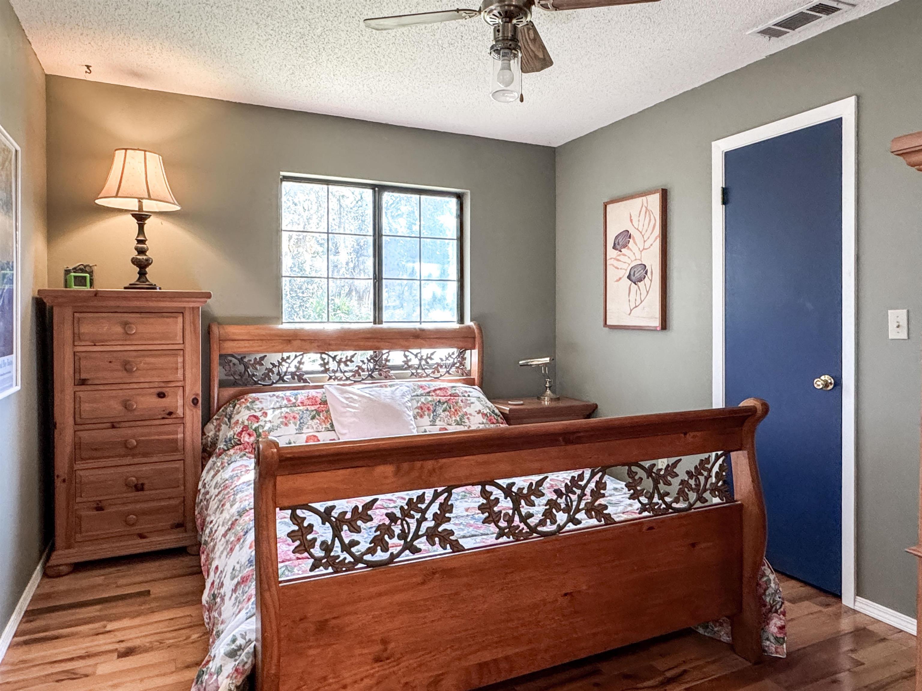 Furnished bedroom with a carved wooden bed, floral bedding, and a blue door beside the window.