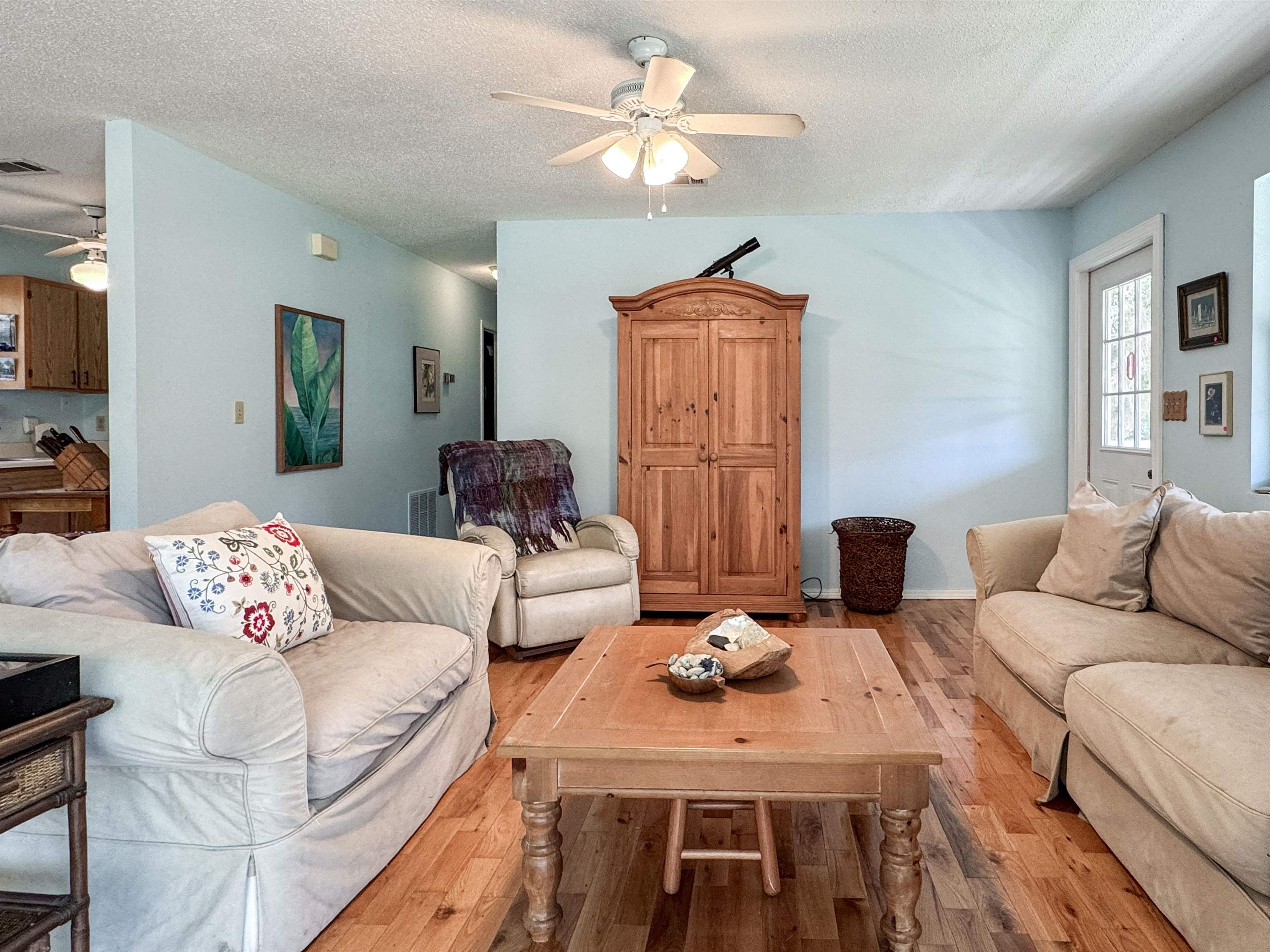 Living room with pale blue walls, hardwood floors, light sofas, and a tall wooden cabinet.
