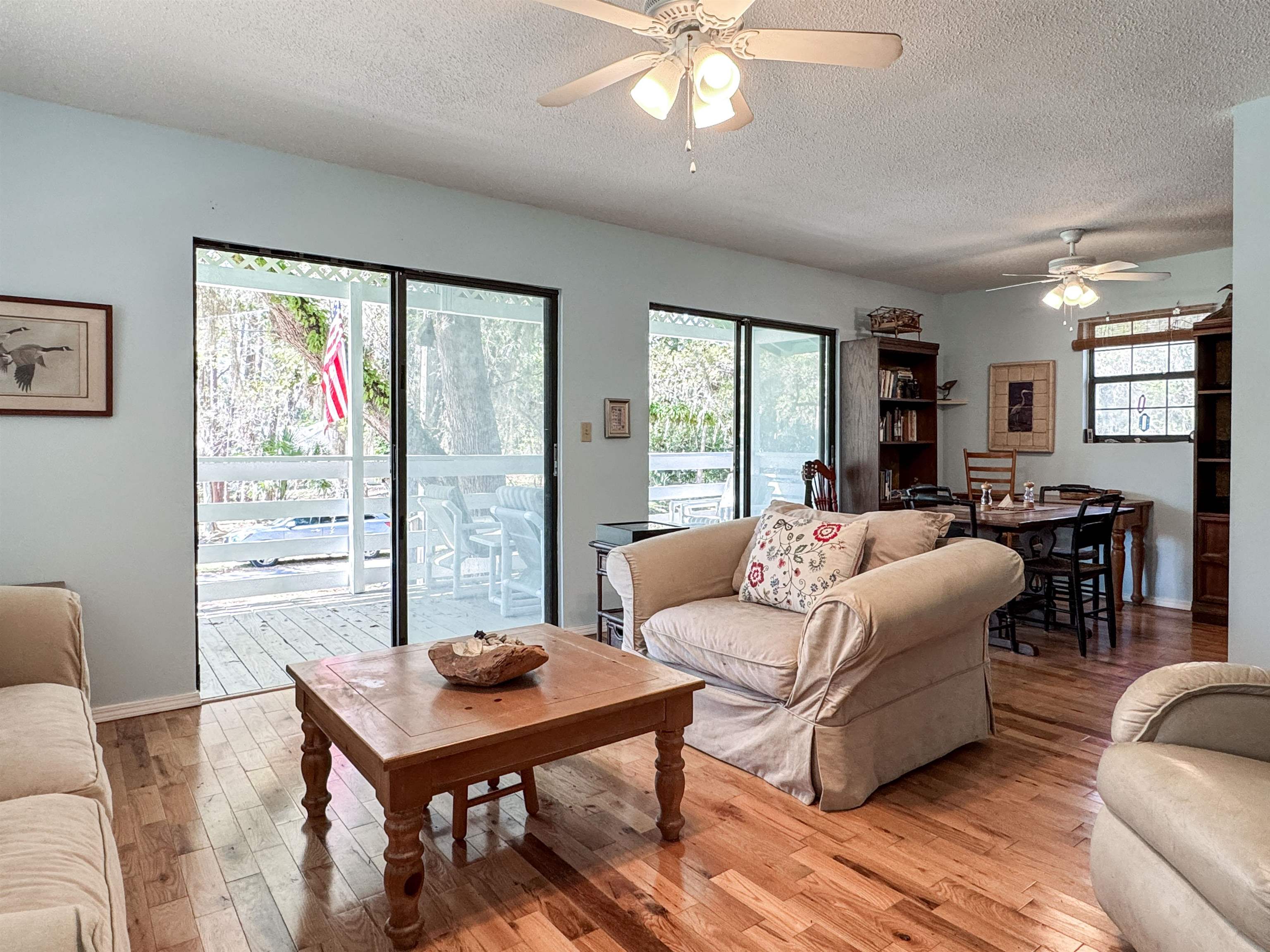 Living and dining room with wood floors and sliding glass doors opening to a tree-lined deck.