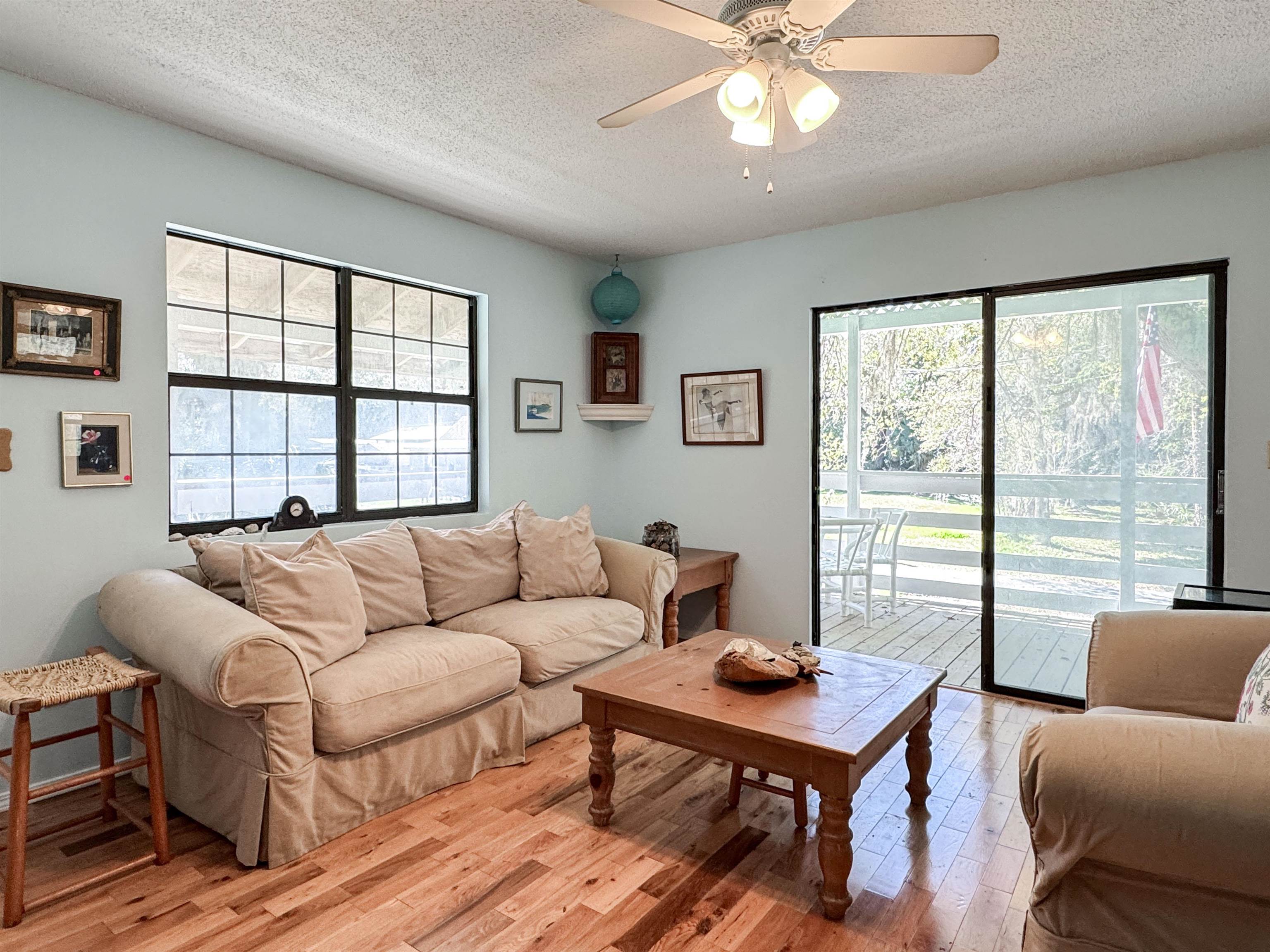 Living room with beige sofas and wood flooring, opening through sliding glass doors to a screened porch.