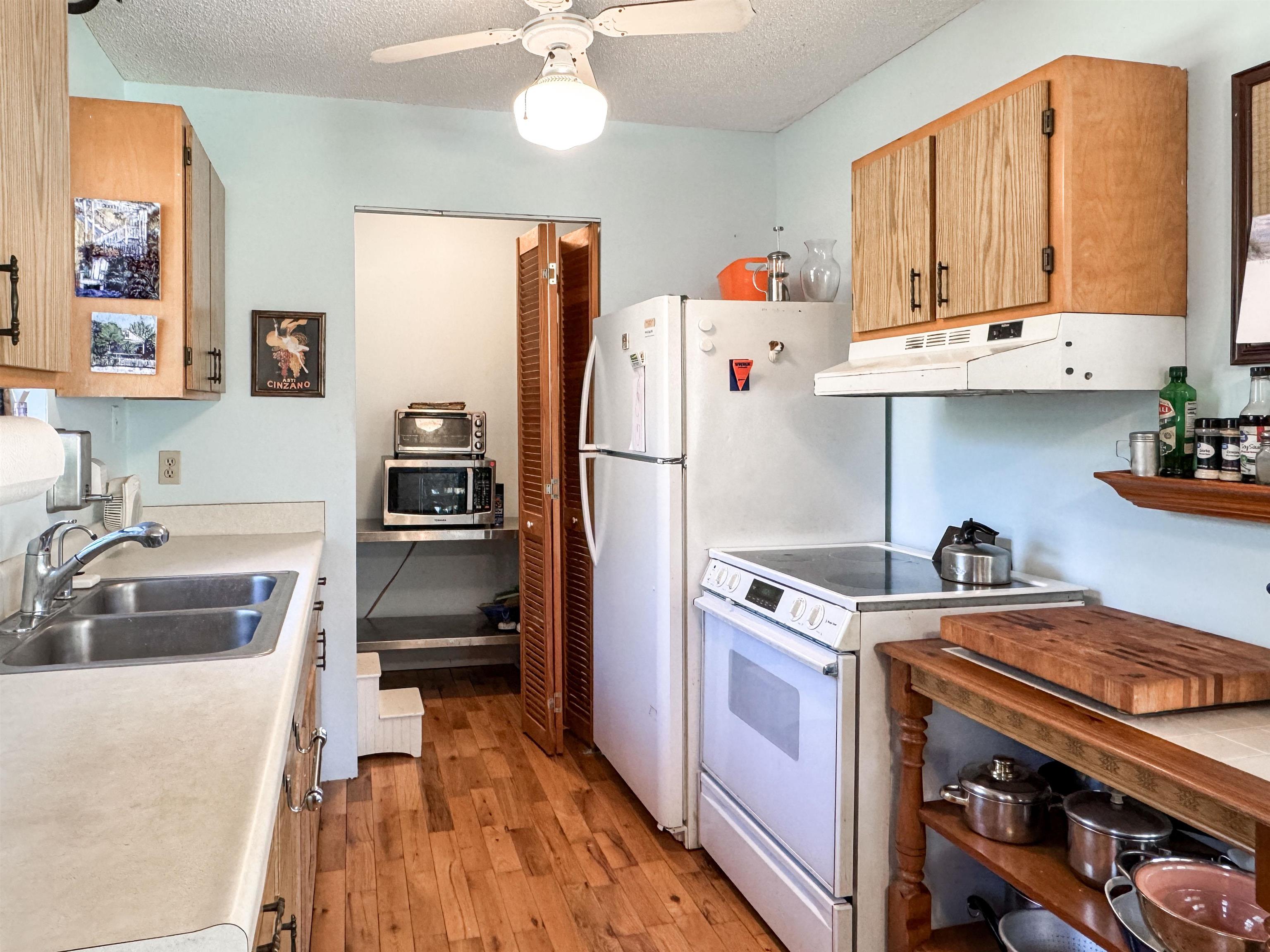 Narrow kitchen with wood cabinets, plank flooring, a white refrigerator and electric range.