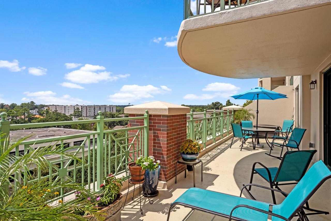 Condo balcony with turquoise lounge chairs, potted plants, and views of nearby buildings and trees.