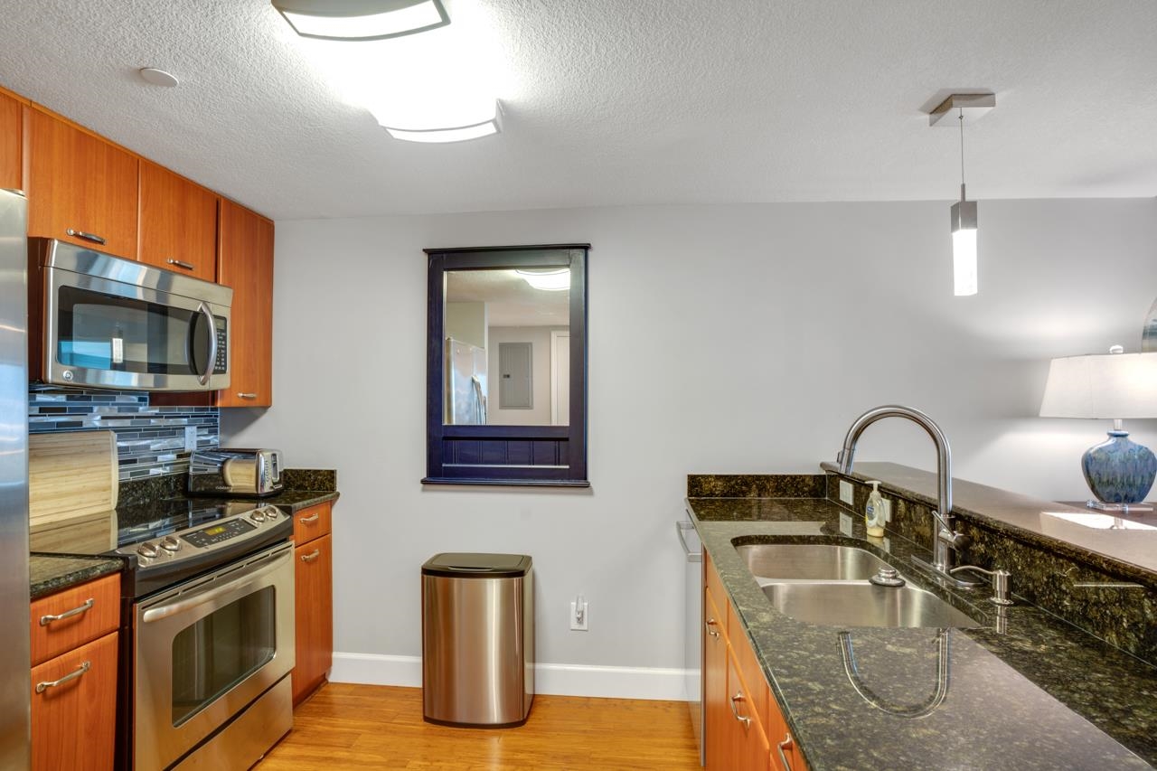 Condo kitchen with wood cabinets, stainless steel appliances, and dark stone countertops.