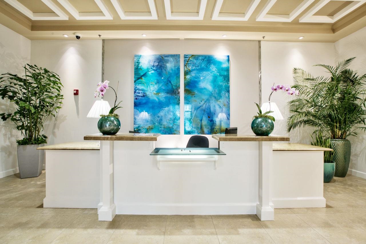 Lobby reception desk with potted plants, blue abstract artwork, and a coffered ceiling.