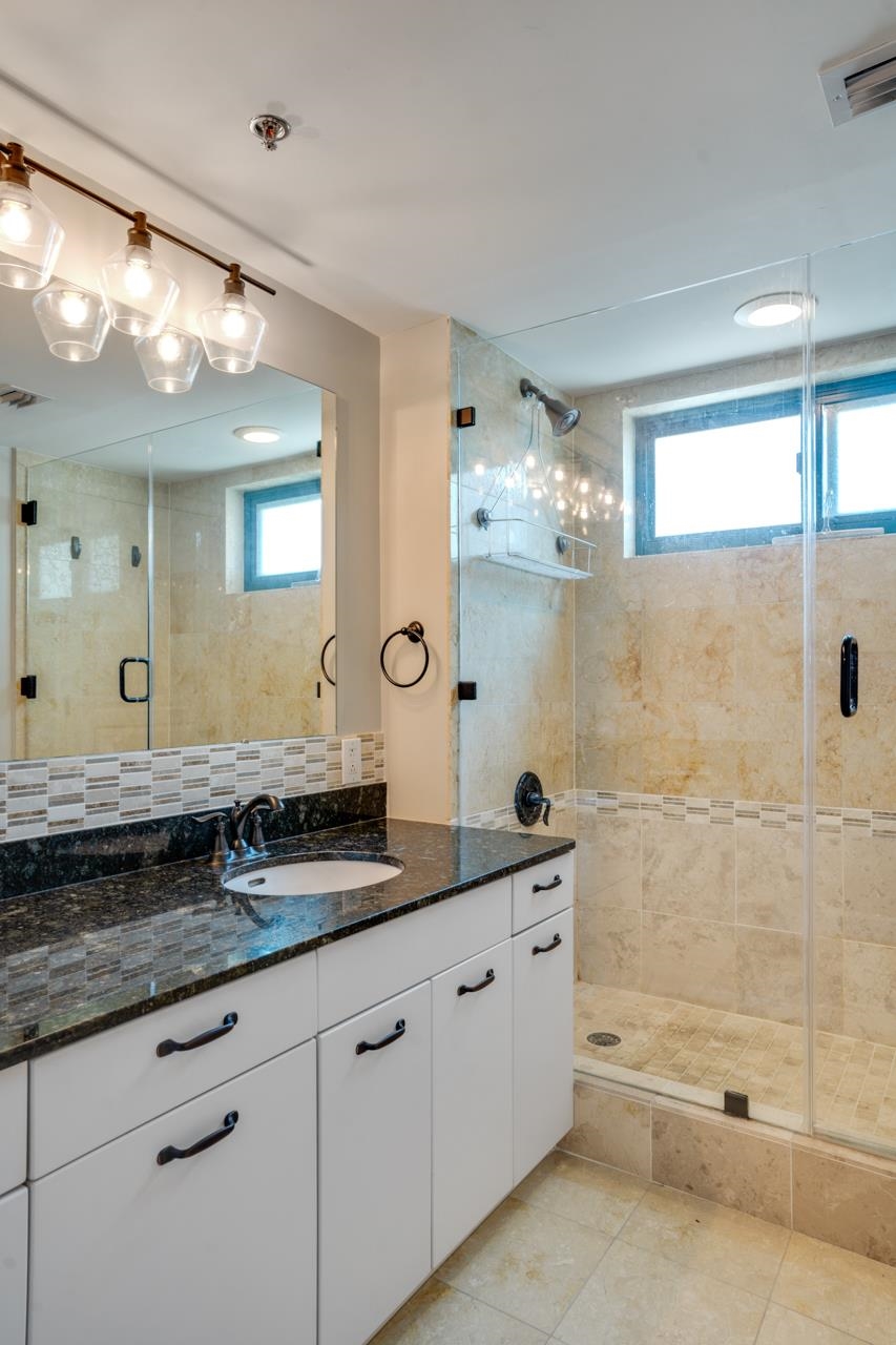Bathroom with a white vanity and glass-enclosed beige tile shower.