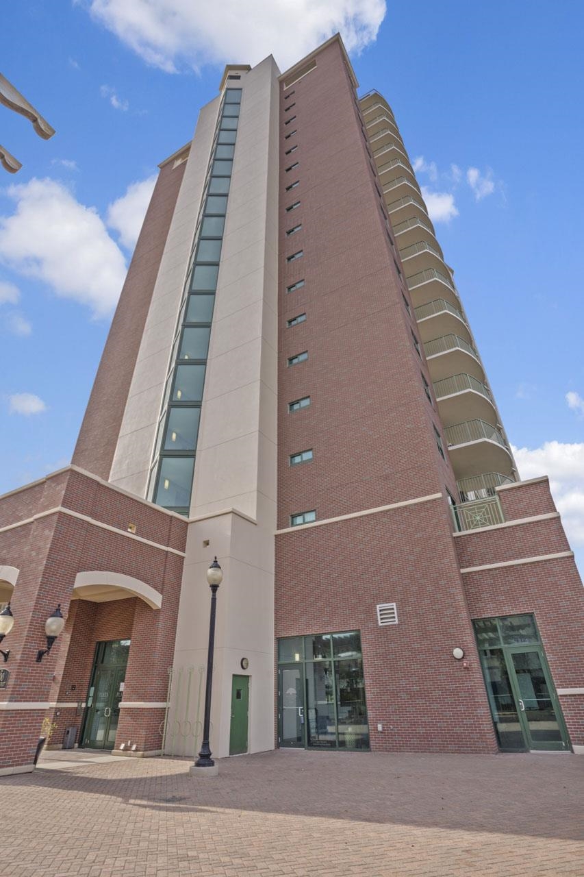 Brick-and-concrete residential tower with stacked balconies and a glass-fronted street-level entrance.