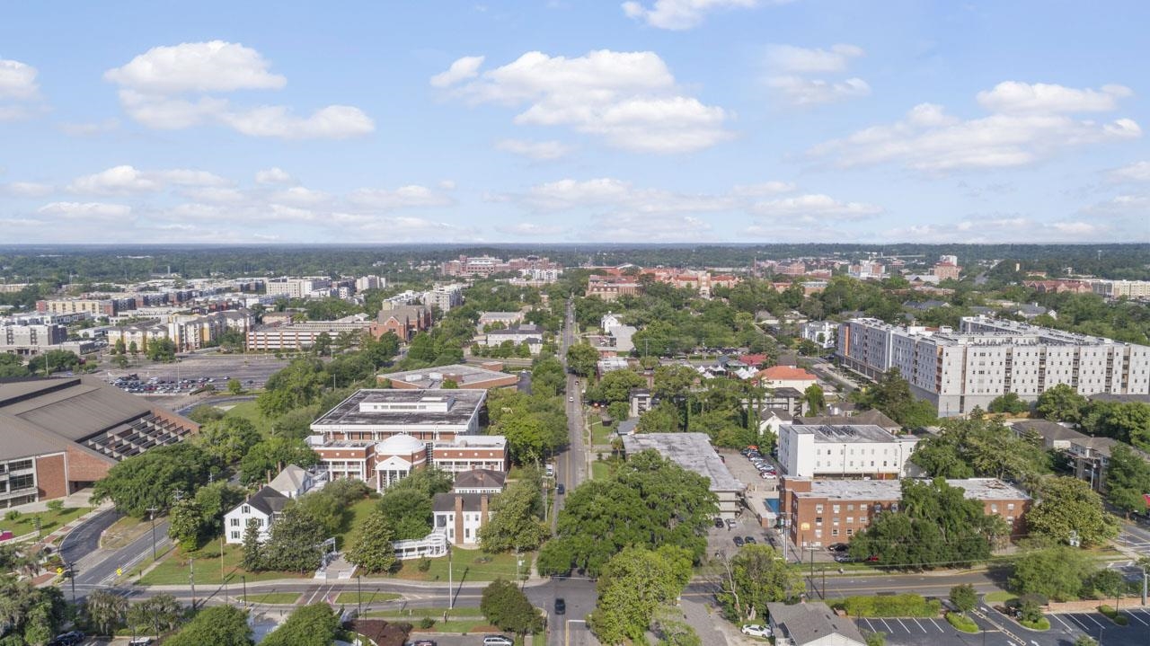 Aerial city view with leafy streets, mid-rise buildings, and a broad partly cloudy sky.