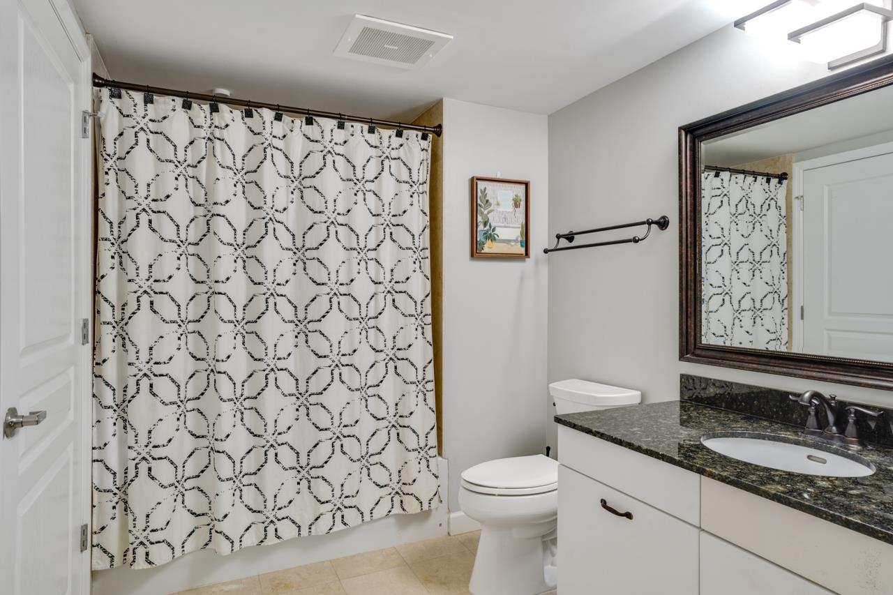 Bathroom with patterned shower curtain, toilet, and white vanity with dark stone countertop.