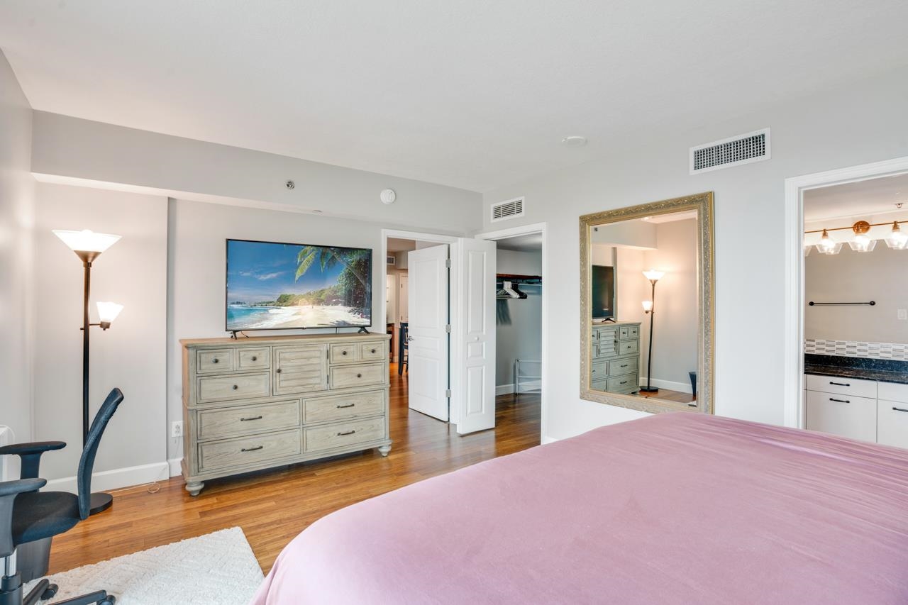 Furnished bedroom with a pink bedspread, hardwood floors, and a dresser topped by a television.