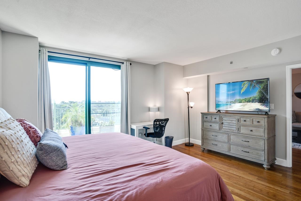 Bedroom with mauve bedding, balcony doors, a desk, and a dresser with a television.