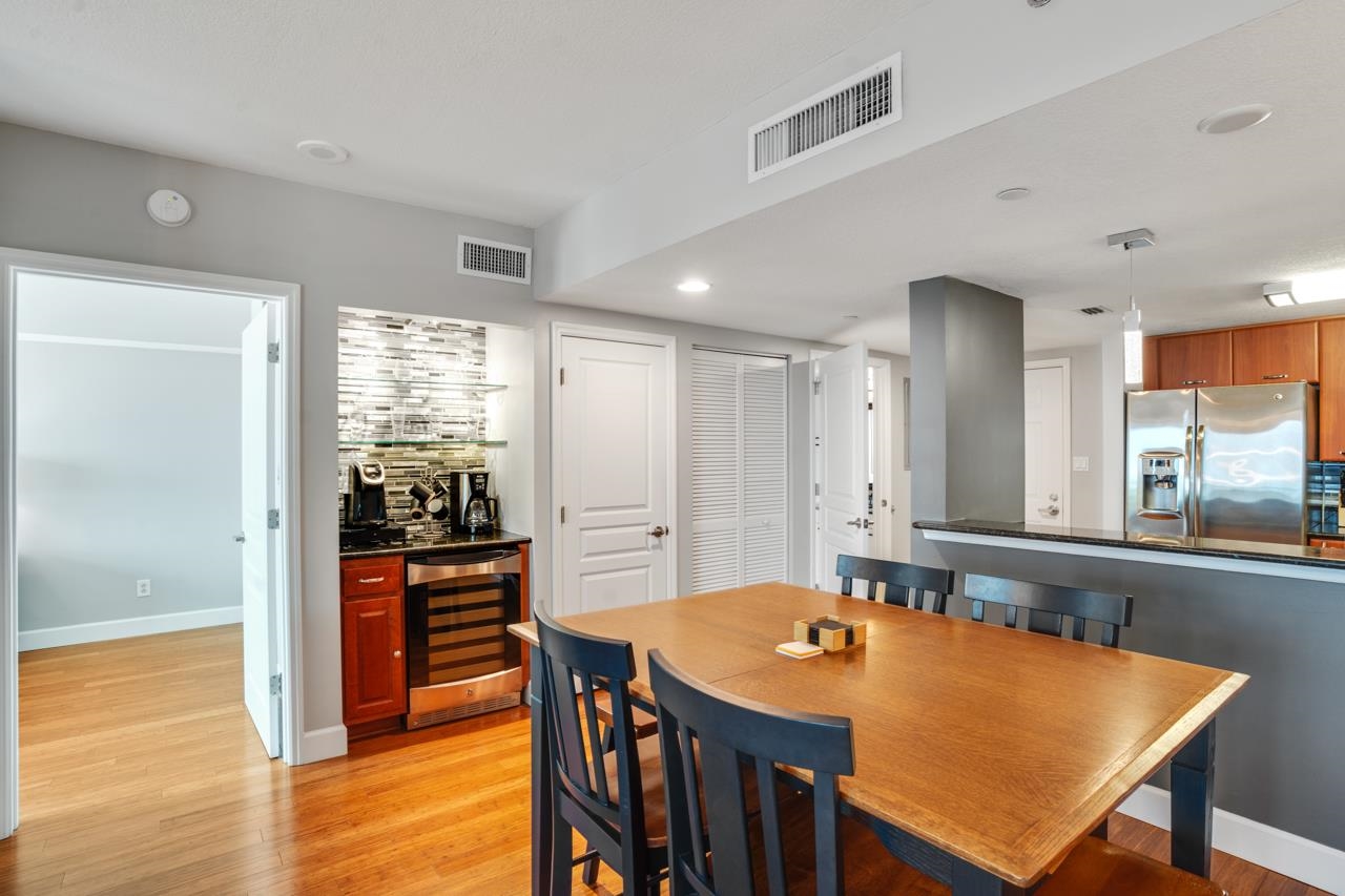 Dining area with a large wooden table beside a kitchen with stainless steel appliances and a beverage station.