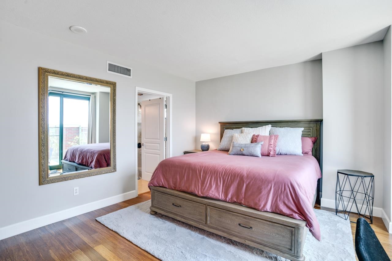 Bedroom with dusty rose bedding, a dark wood storage bed, and a gold-framed mirror.
