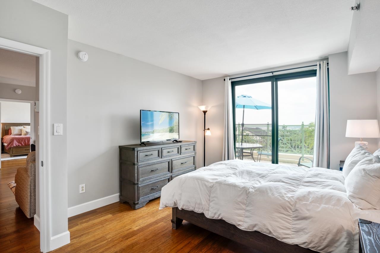 Bedroom with white bedding, a dark wood dresser, and sliding doors opening to a balcony.