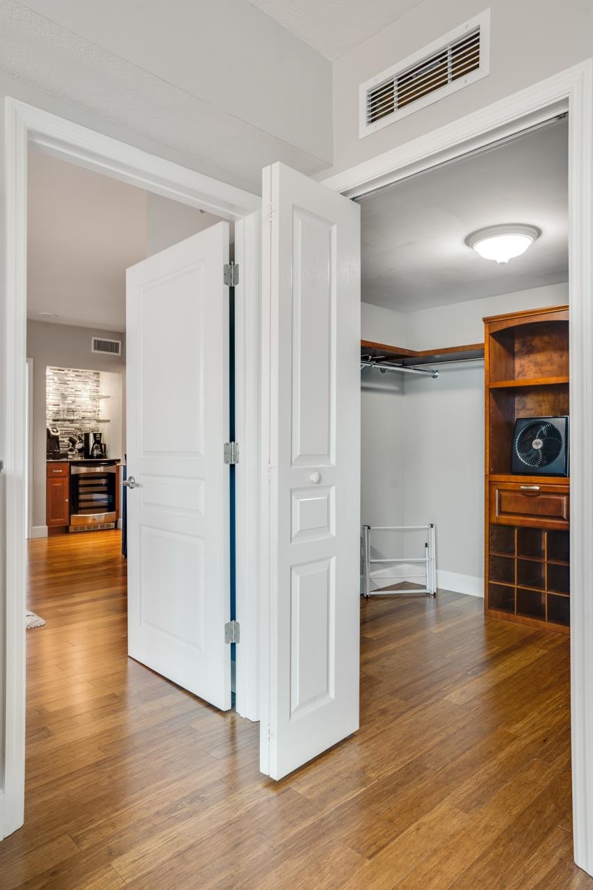 Open closet with hanging rods and built-in wooden shelving beside a glimpse of the kitchen.