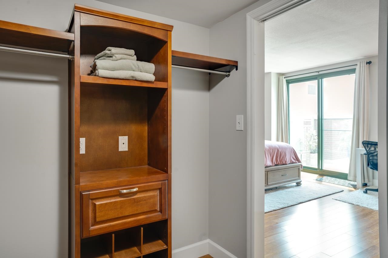 Walk-in closet with wooden built-ins and folded towels, opening onto a bedroom with a balcony door.