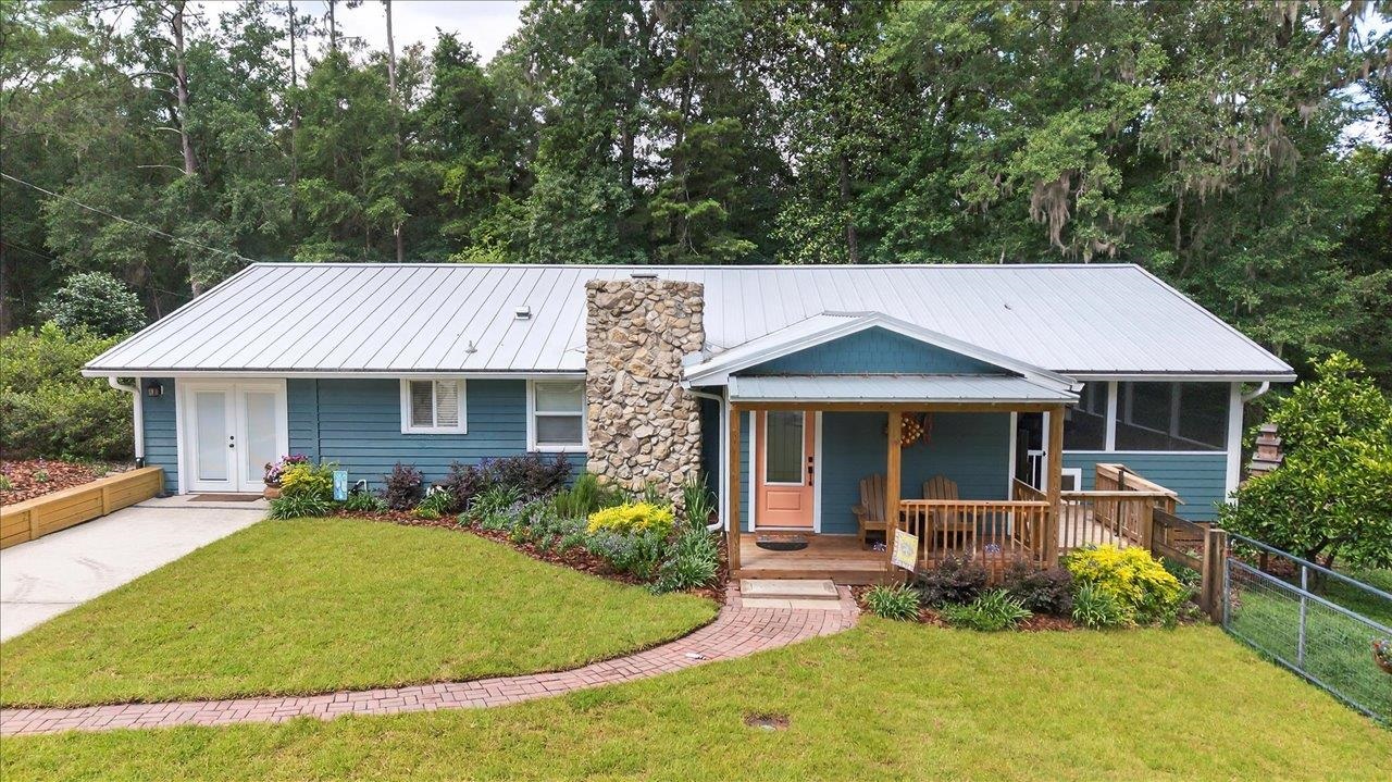 Blue single-story home with a stone chimney, covered porch, and curved brick walkway.